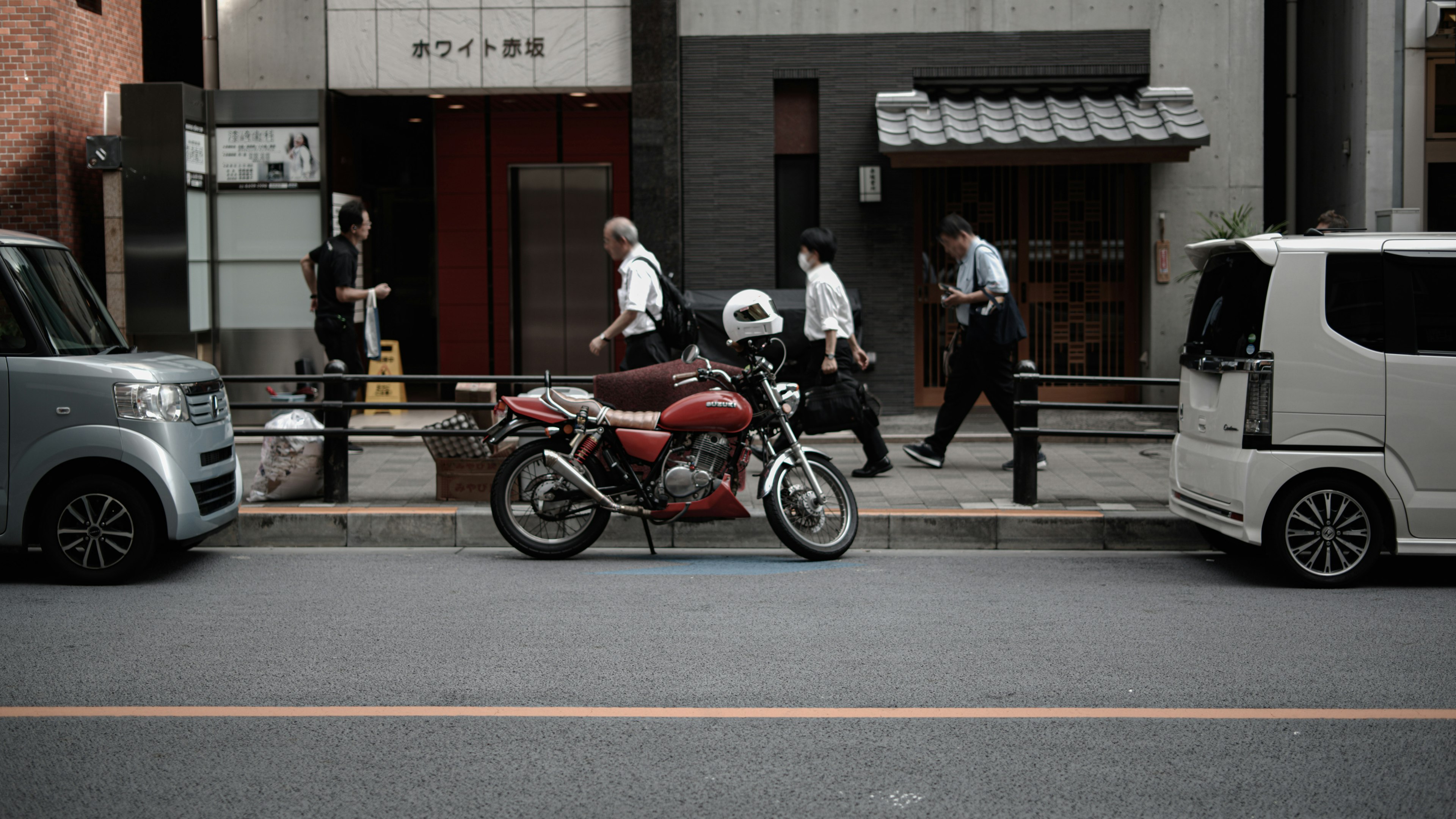 Straßenszene in Tokio mit einem geparkten roten Motorrad und Fußgängern