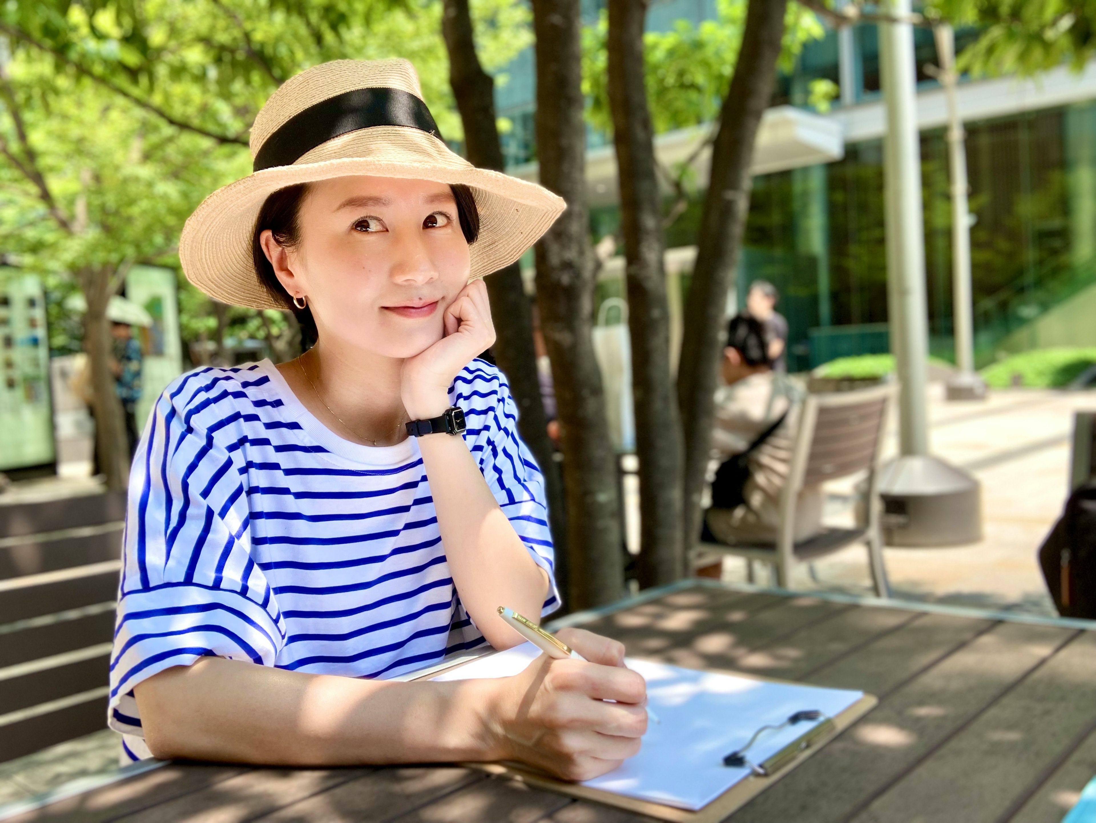 A woman in a striped shirt and hat sitting at a table outdoors deep in thought