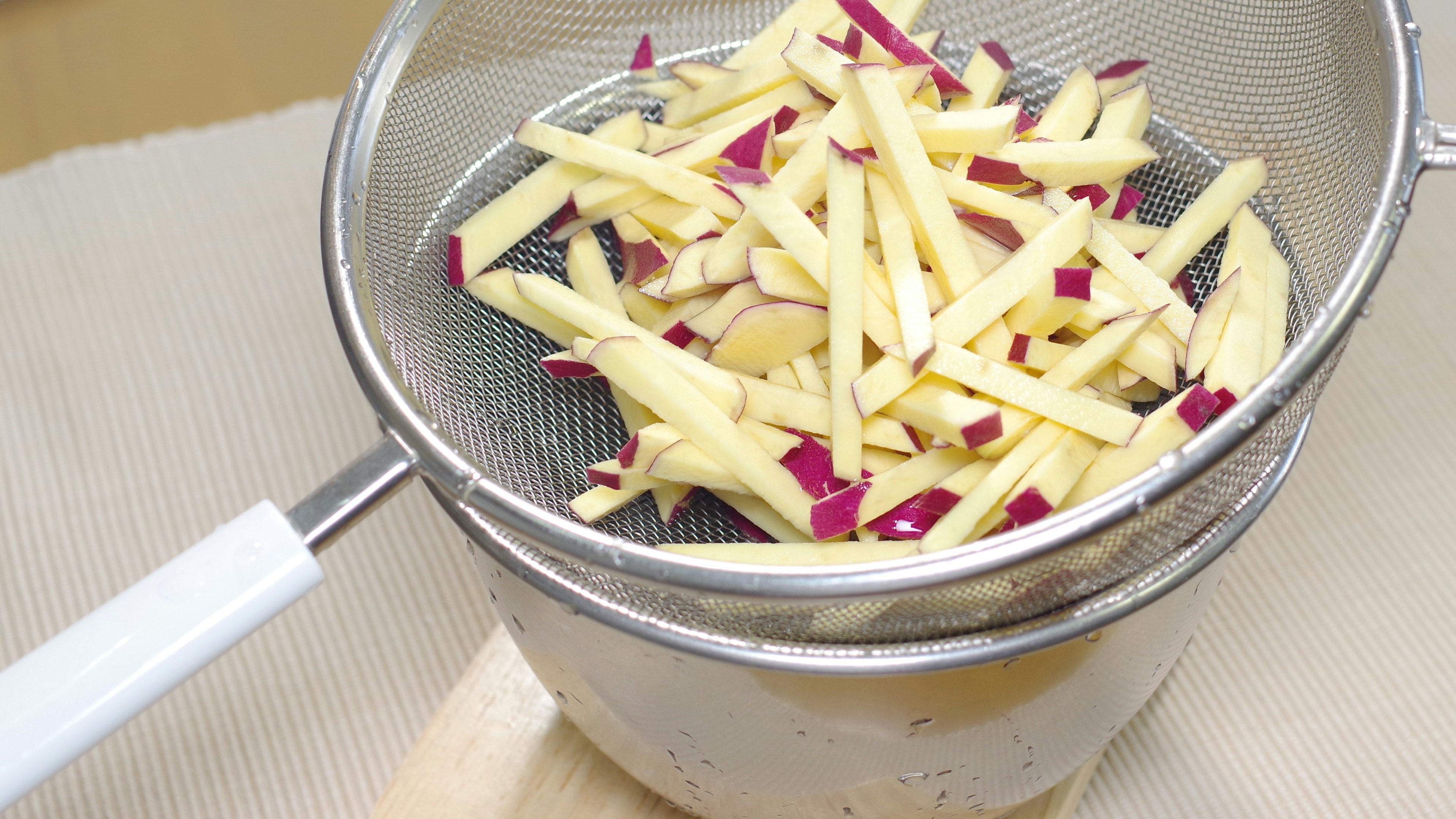 Sliced apple strips in a strainer above a bowl