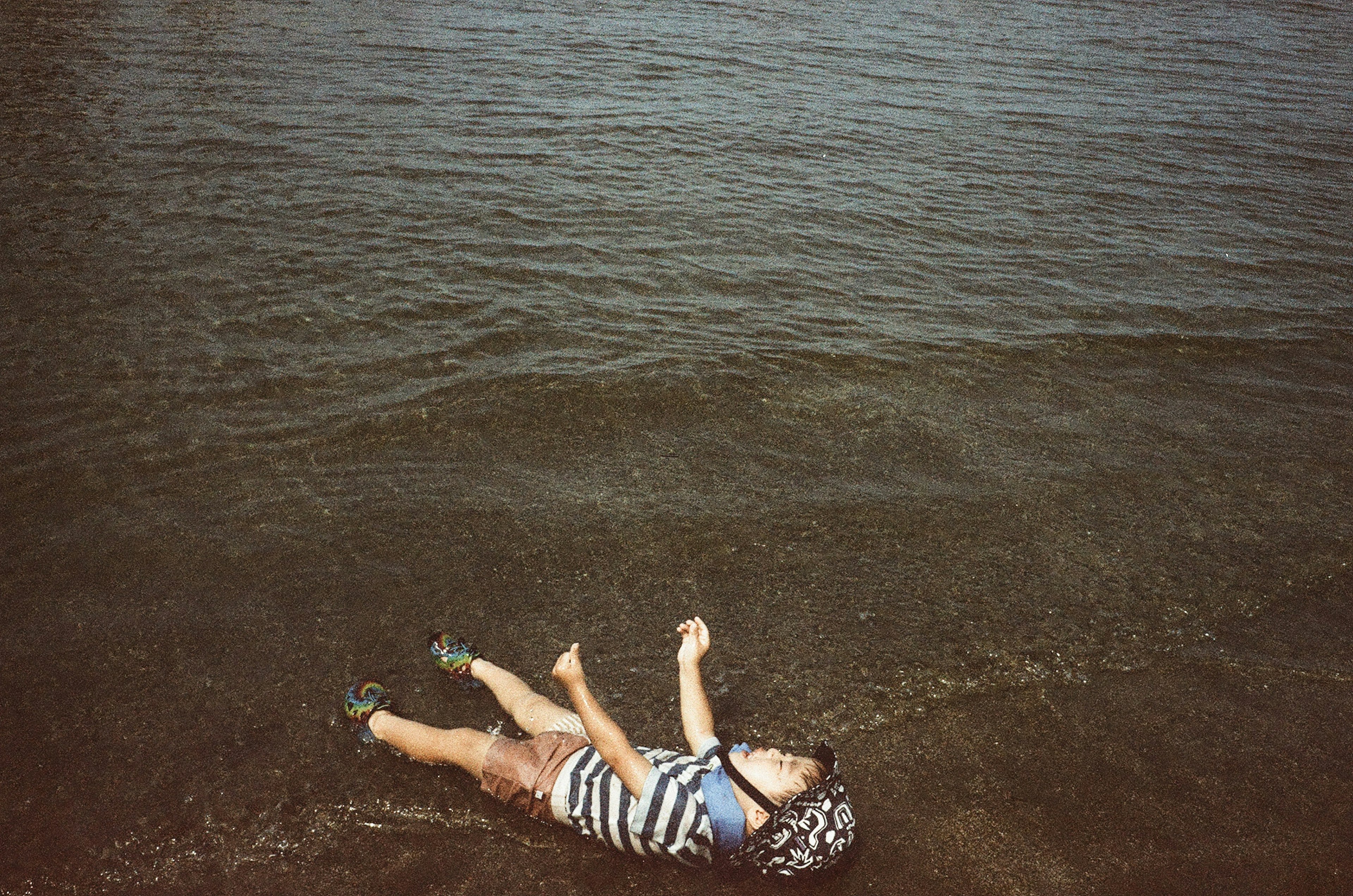 Child lying on the water's edge wearing a striped swimsuit