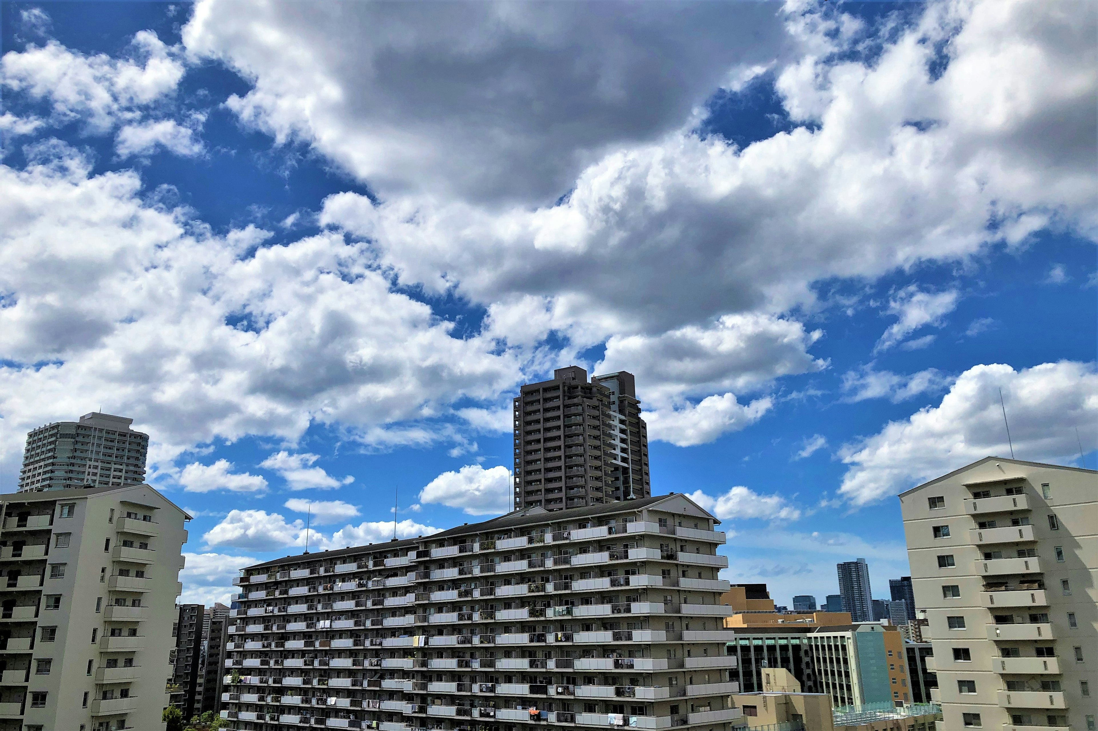 Pemandangan perkotaan dengan langit biru dan awan putih menampilkan gedung tinggi dan apartemen