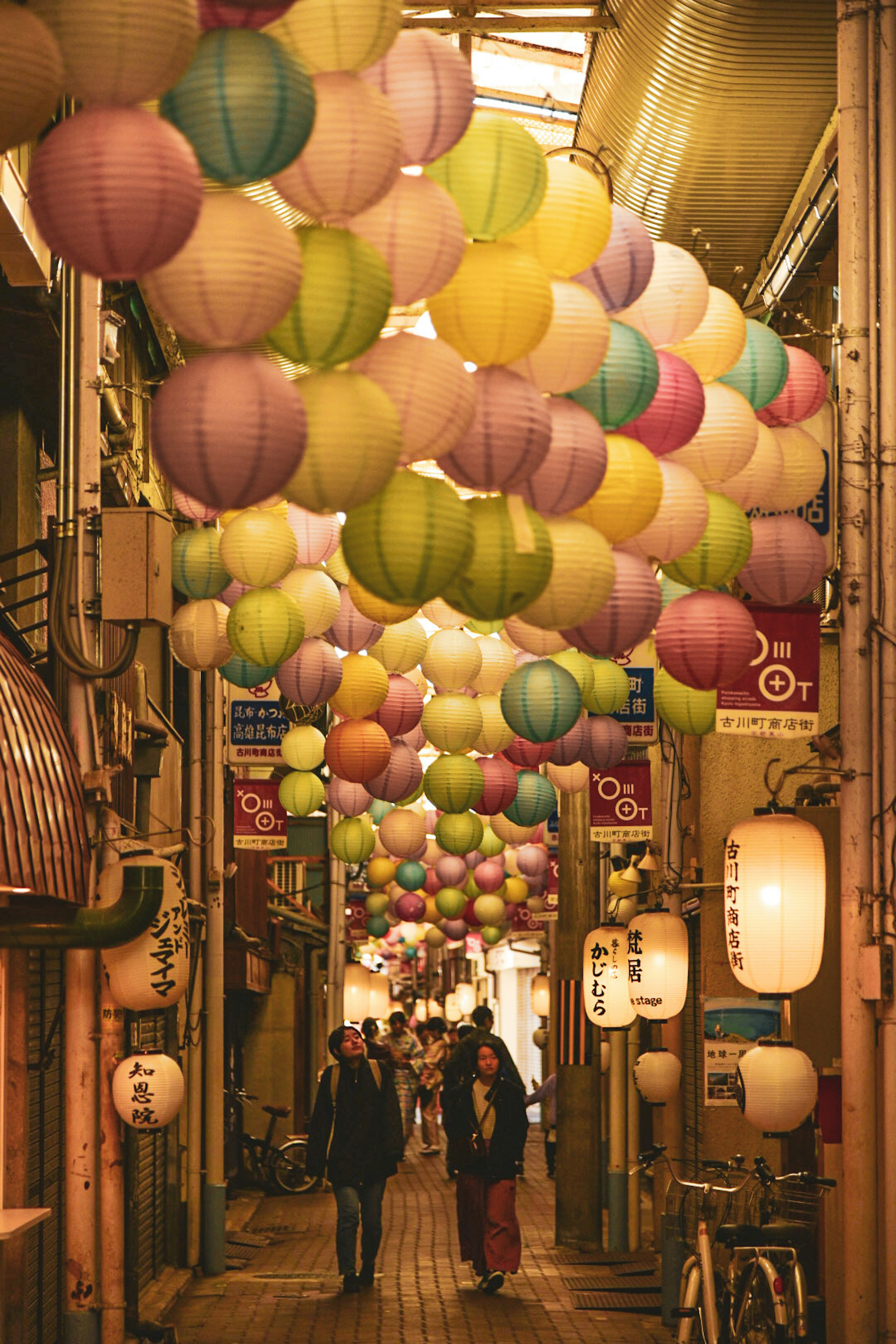 People walking through a narrow street adorned with colorful lanterns