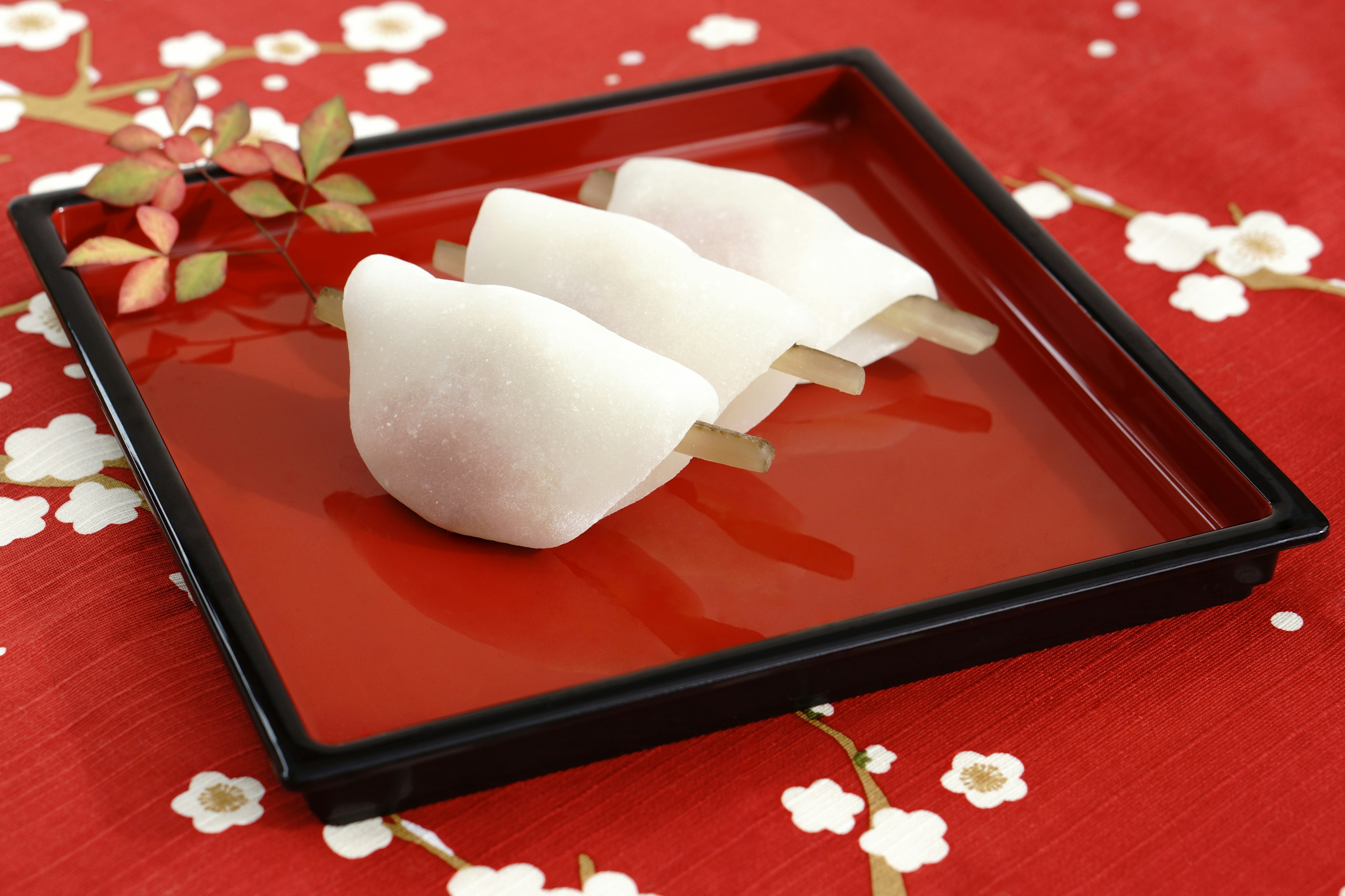 Un plato hermoso con wagashi blancos sobre un fondo rojo