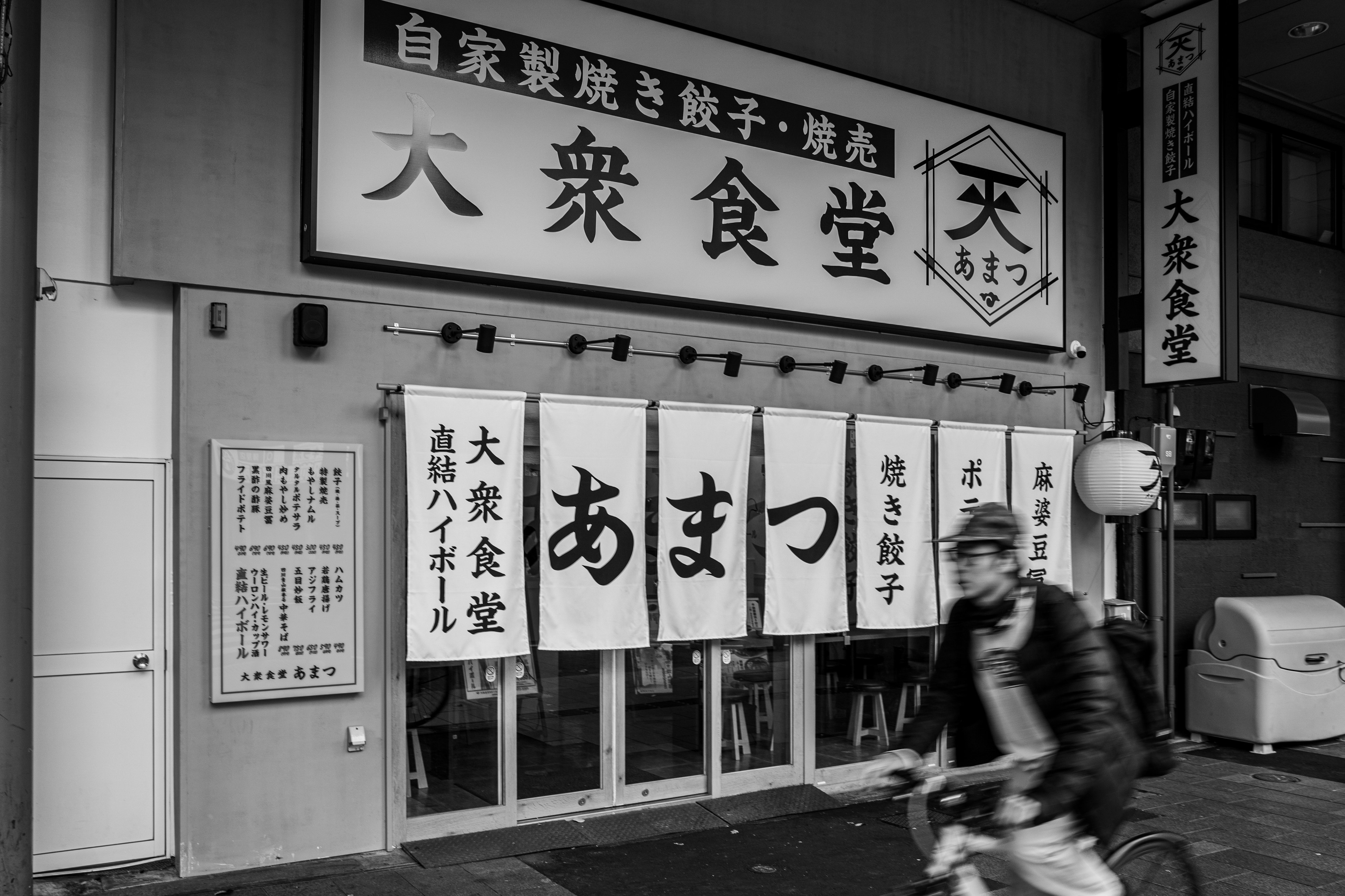 Exterior de restaurante en blanco y negro con letreros y pancartas