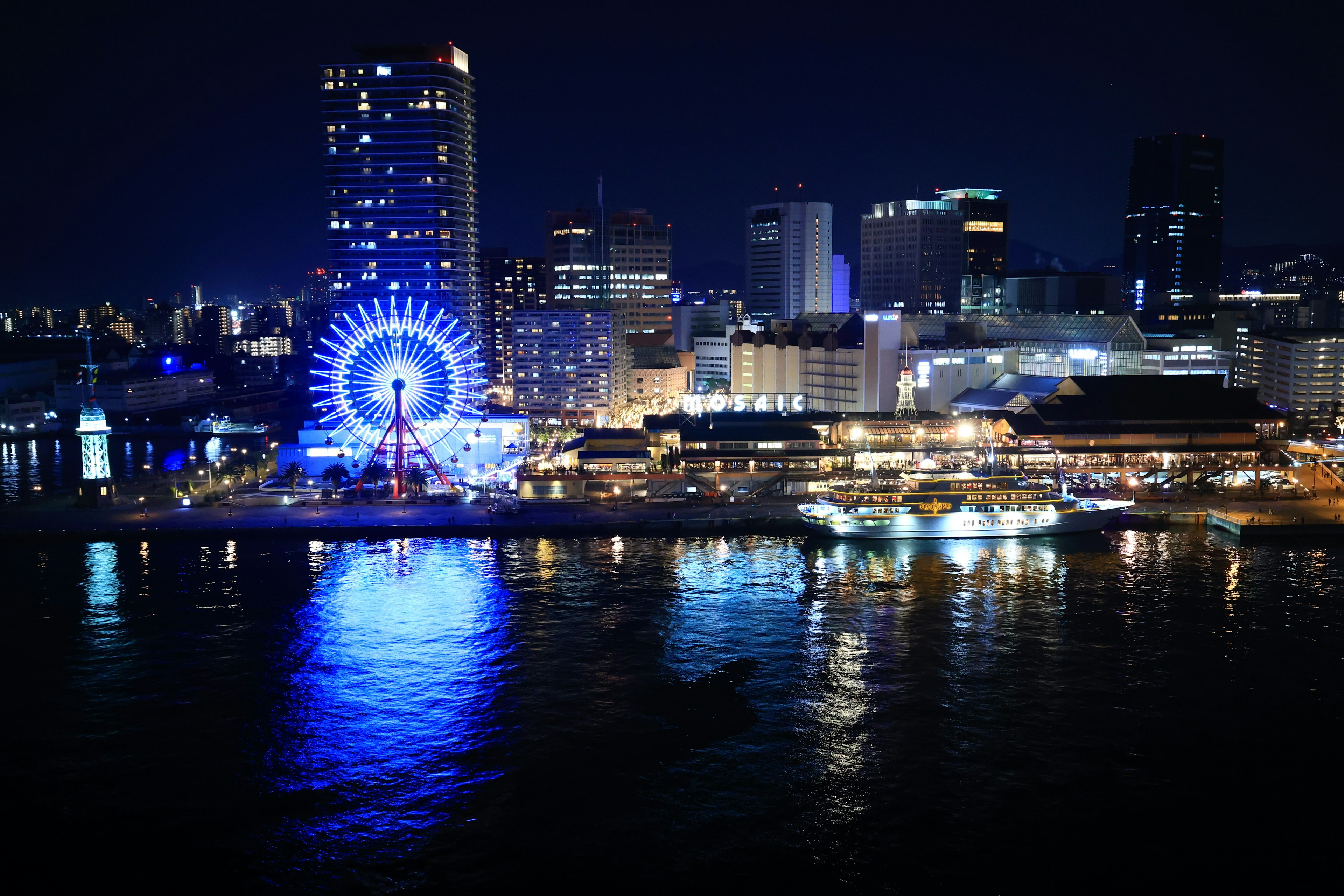 Nighttime cityscape featuring a blue ferris wheel and bright buildings