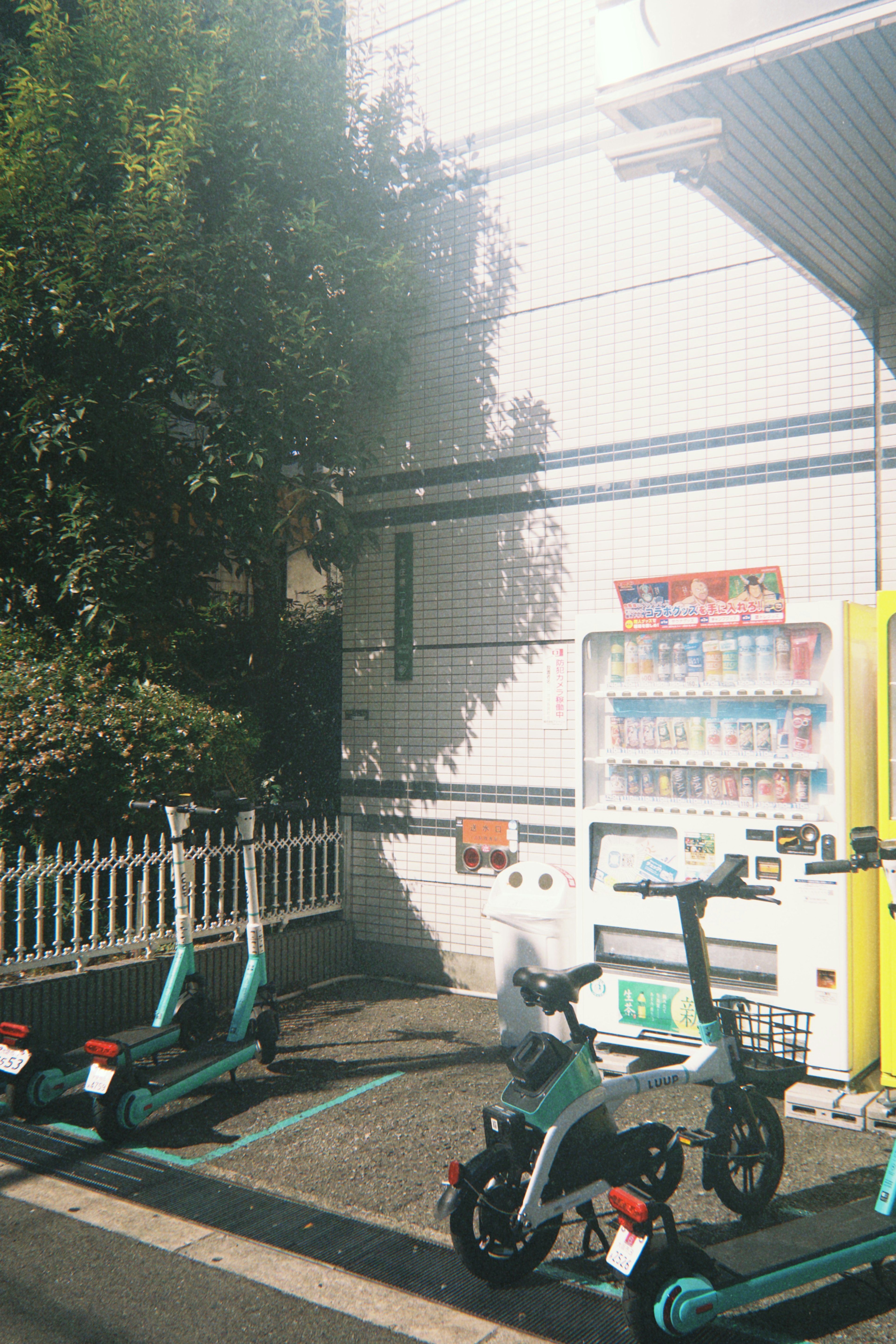 Bicycles and electric scooters parked near a vending machine with greenery in the background