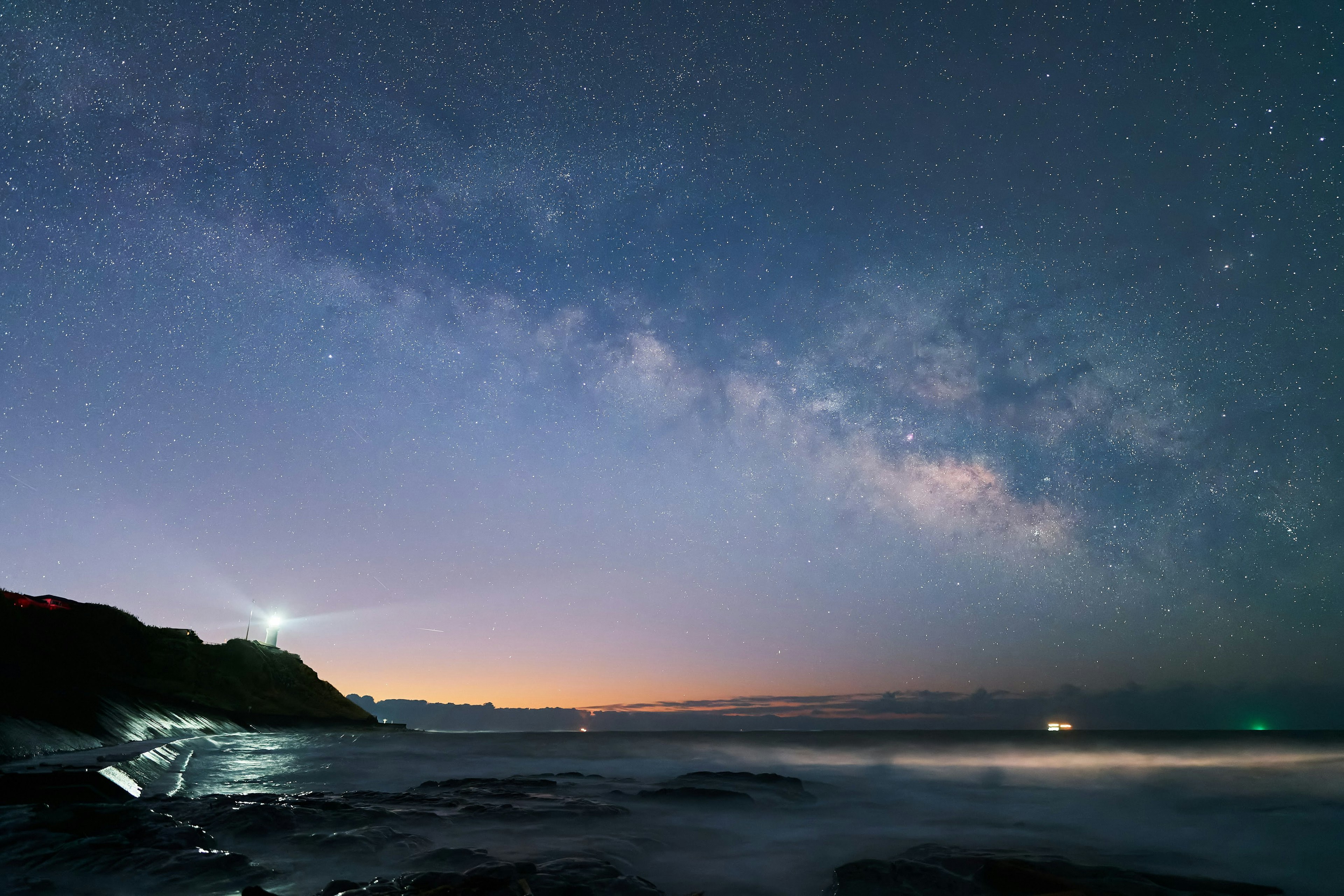 Cielo notturno con la Via Lattea e costa con un faro