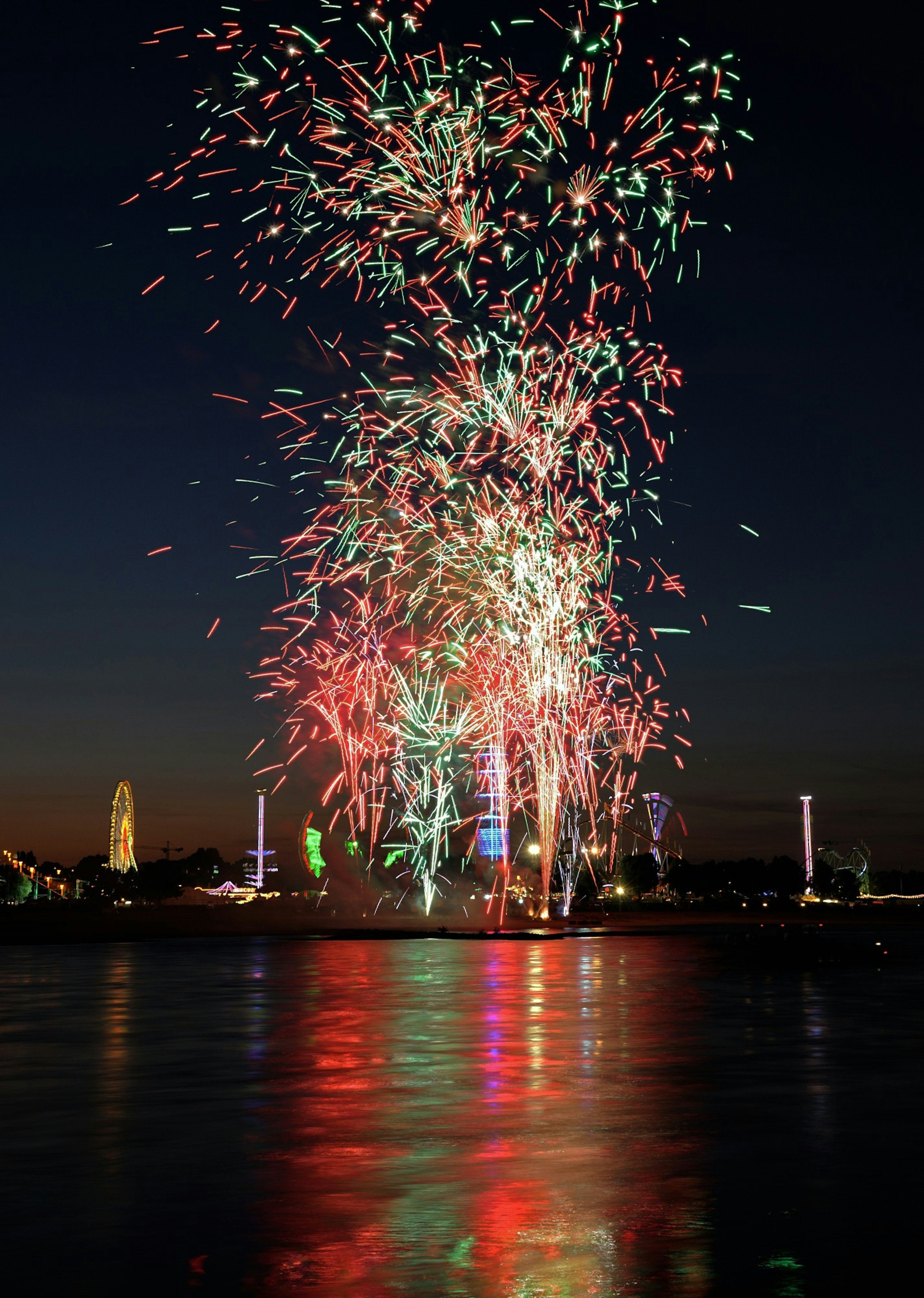 Fuegos artificiales coloridos estallando en el cielo nocturno con reflejos en el agua