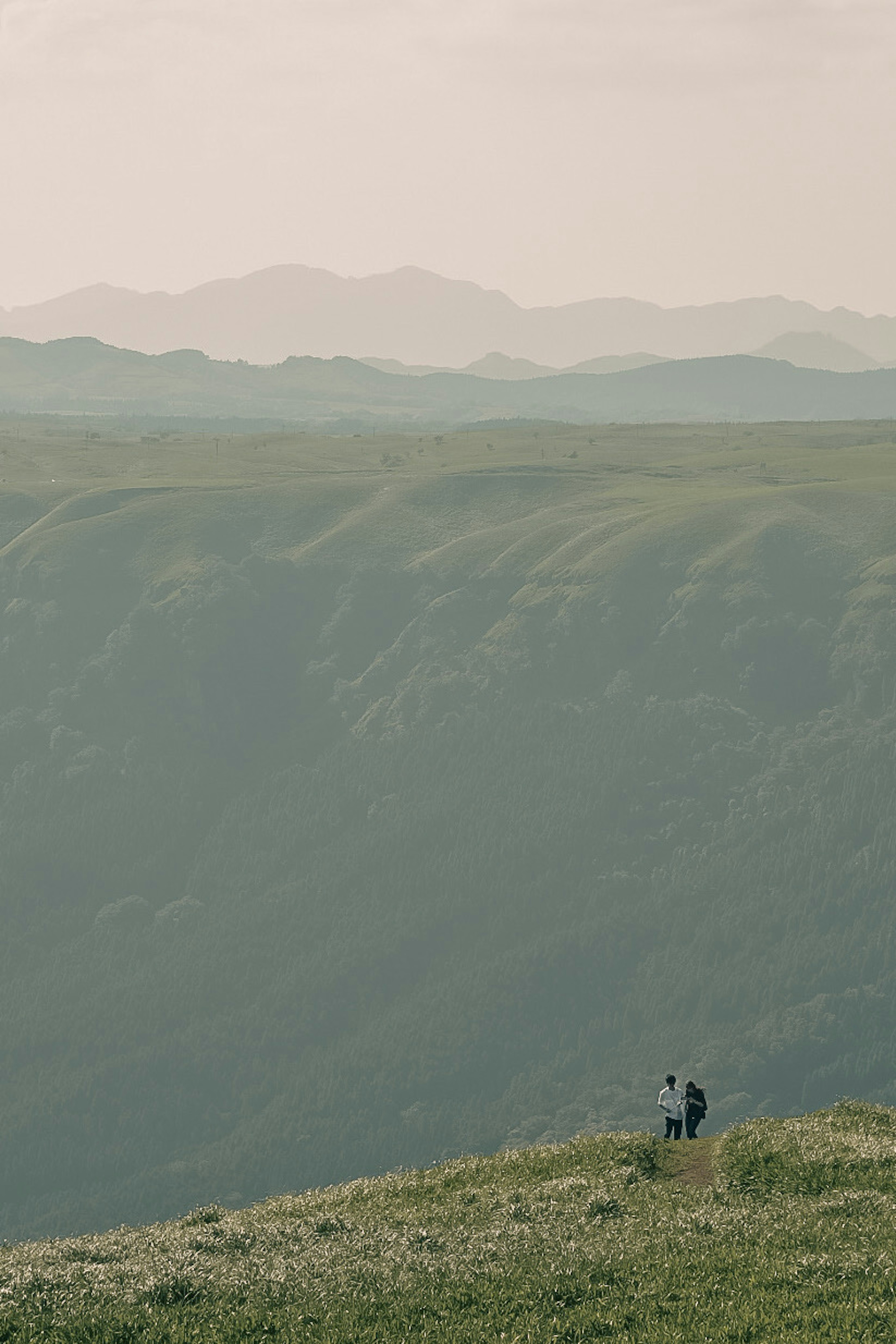 Due figure in piedi su una vasta collina verde con montagne lontane