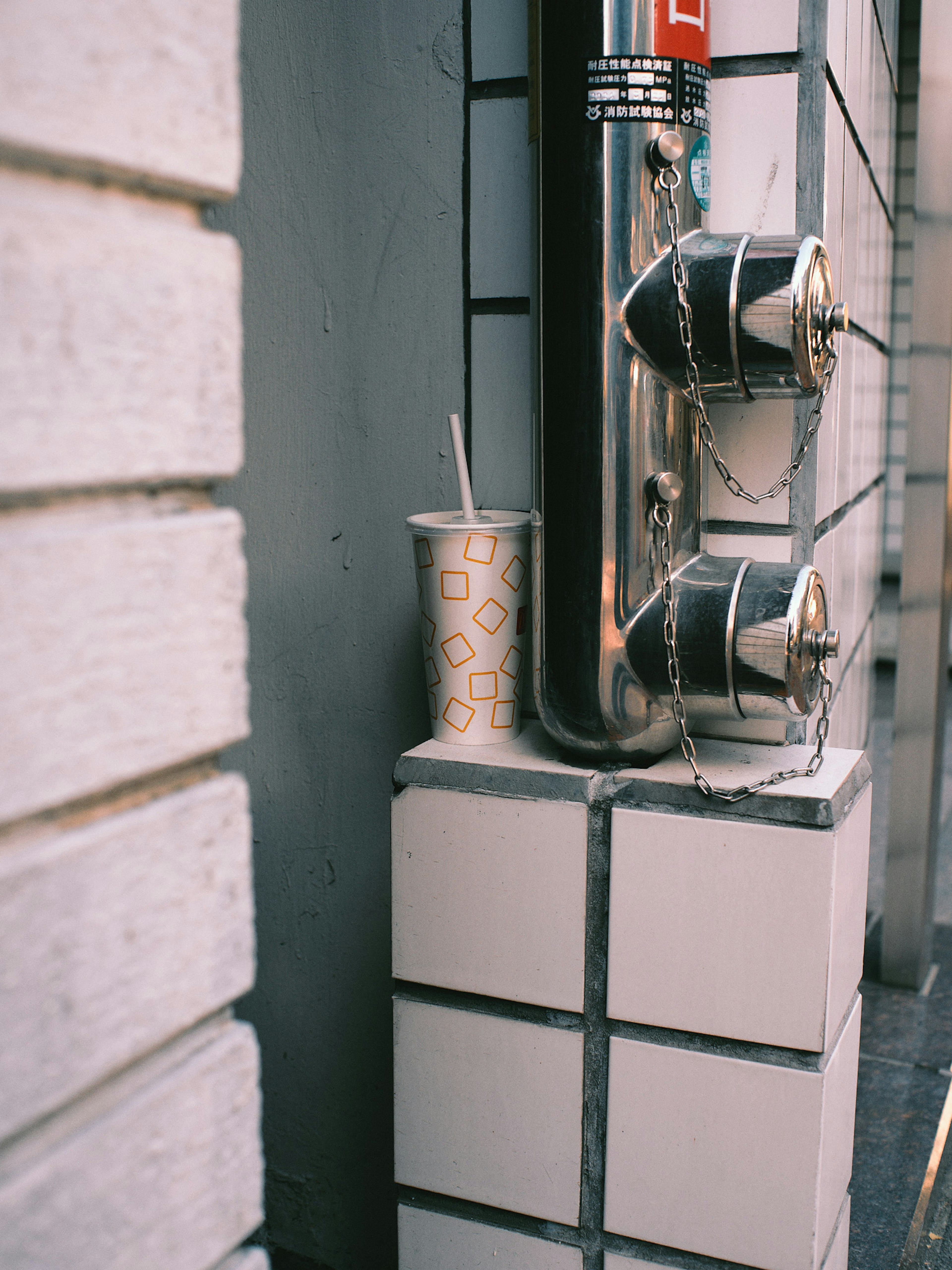 Vaso de plástico apoyado contra una pared con tuberías de metal en un entorno urbano