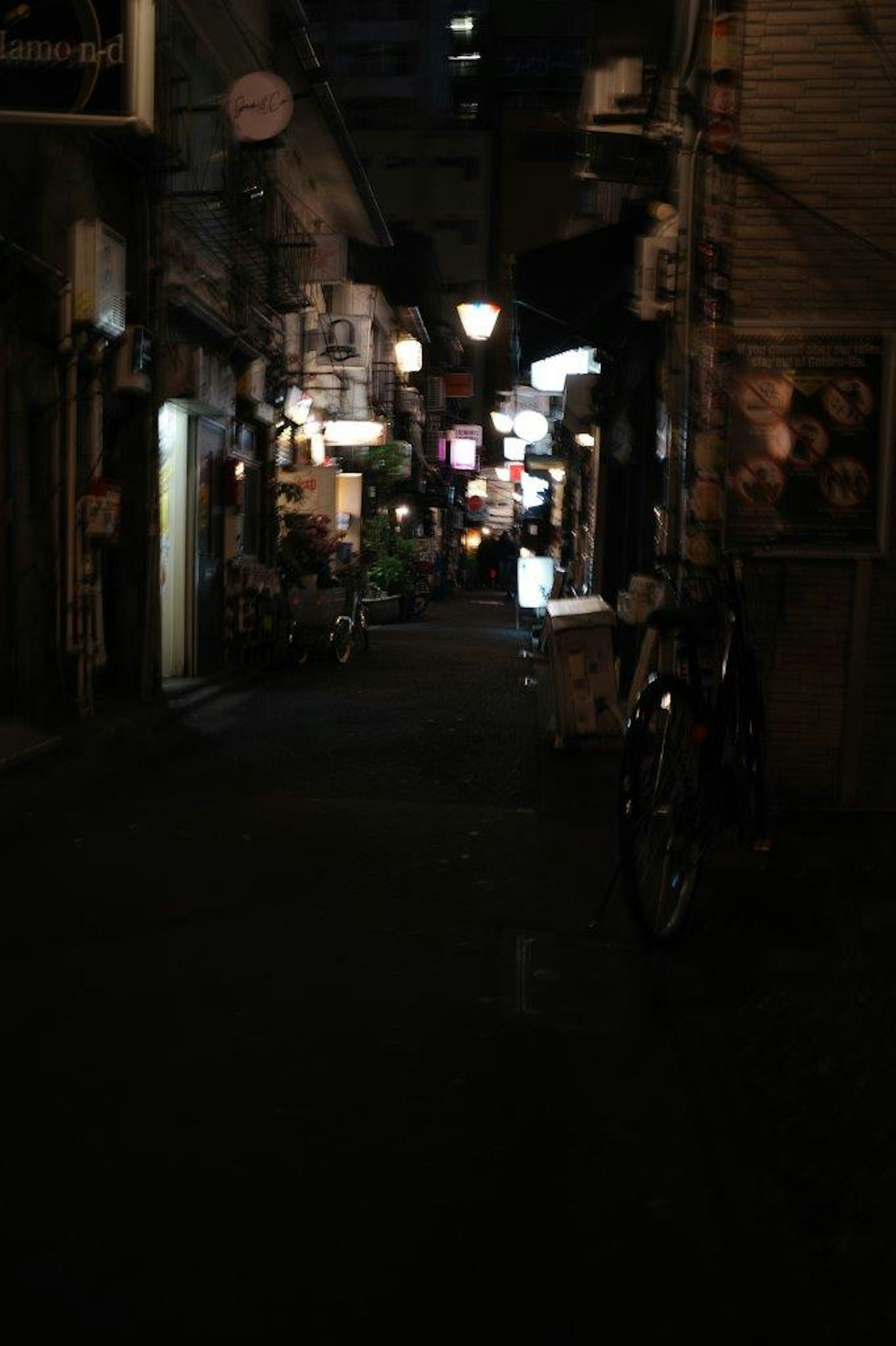 Callejón estrecho iluminado por luces de restaurantes con una bicicleta en primer plano