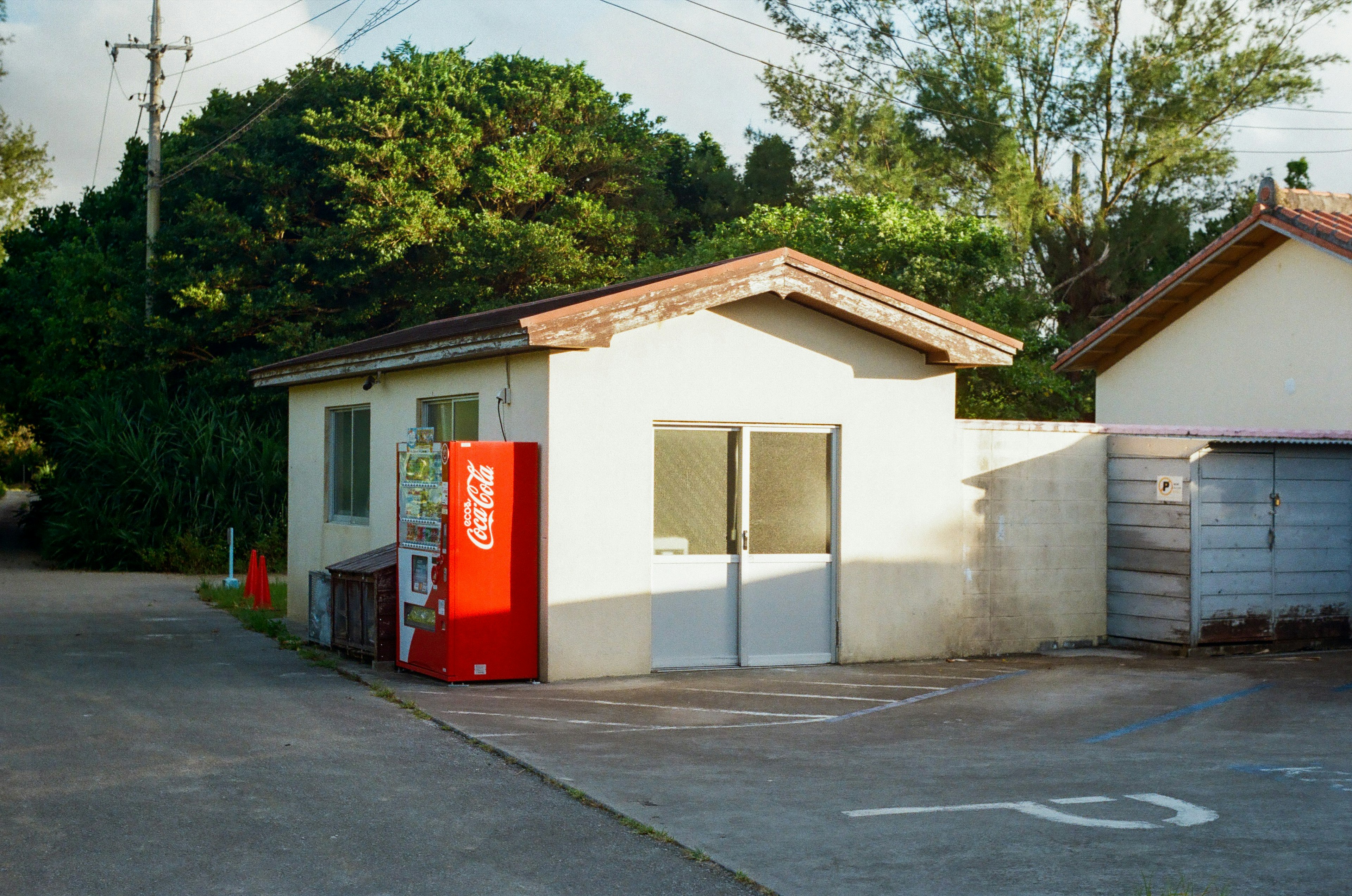 赤い自動販売機のある小さな建物と周囲の緑の風景