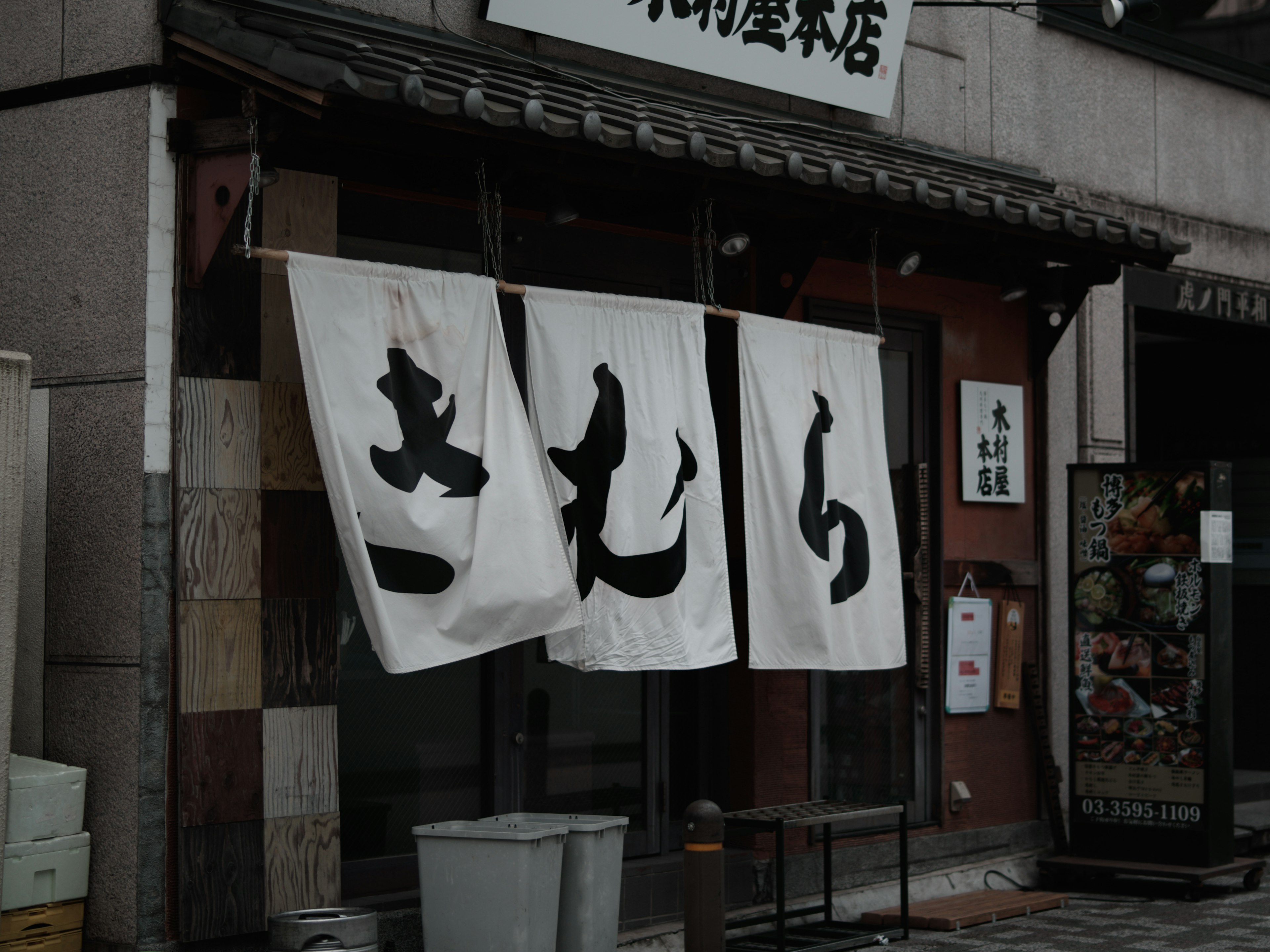 Extérieur d'un magasin japonais avec un noren blanc affichant de grands caractères noirs