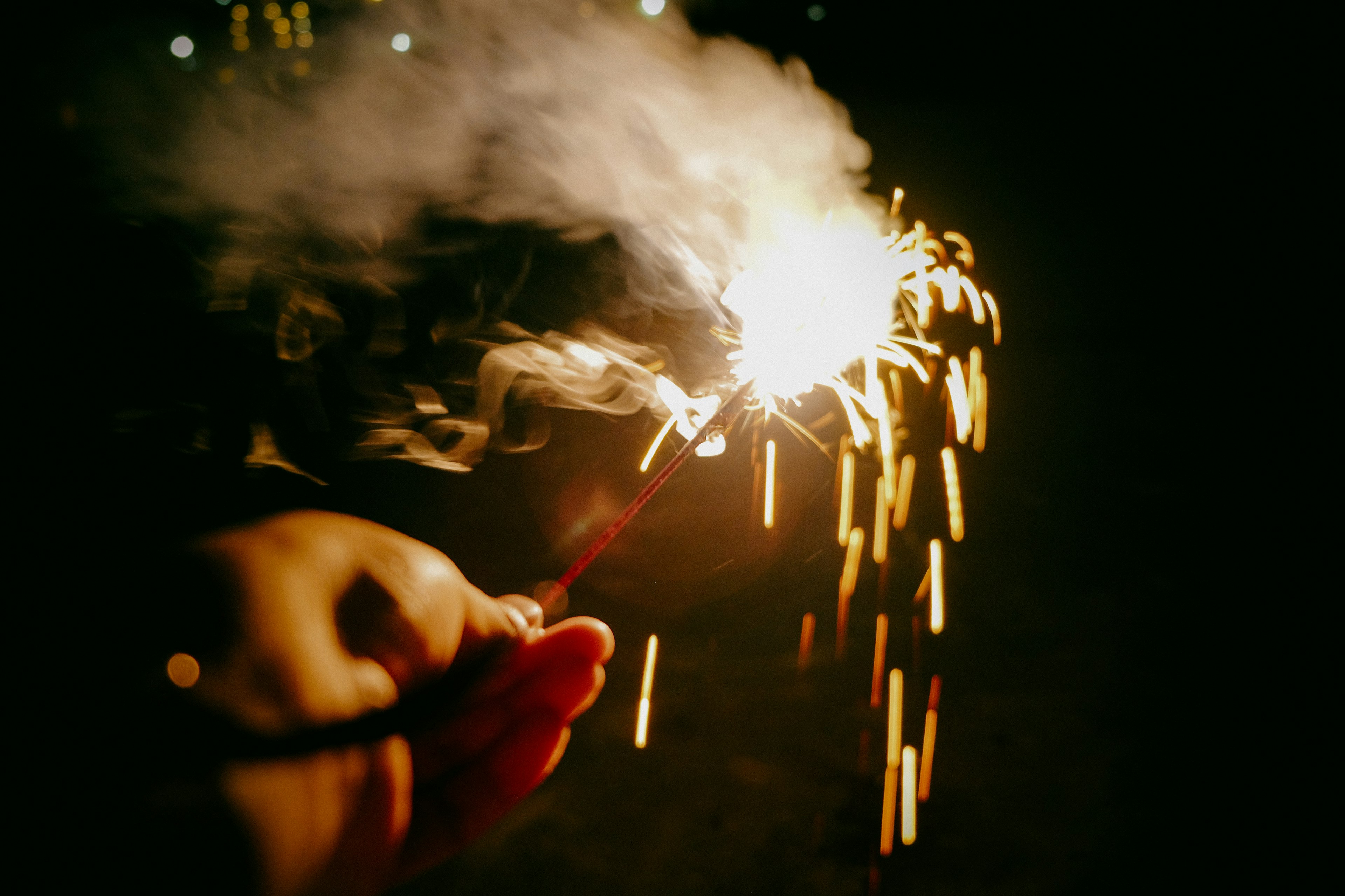 Hand holding a sparkler with sparks and smoke at night