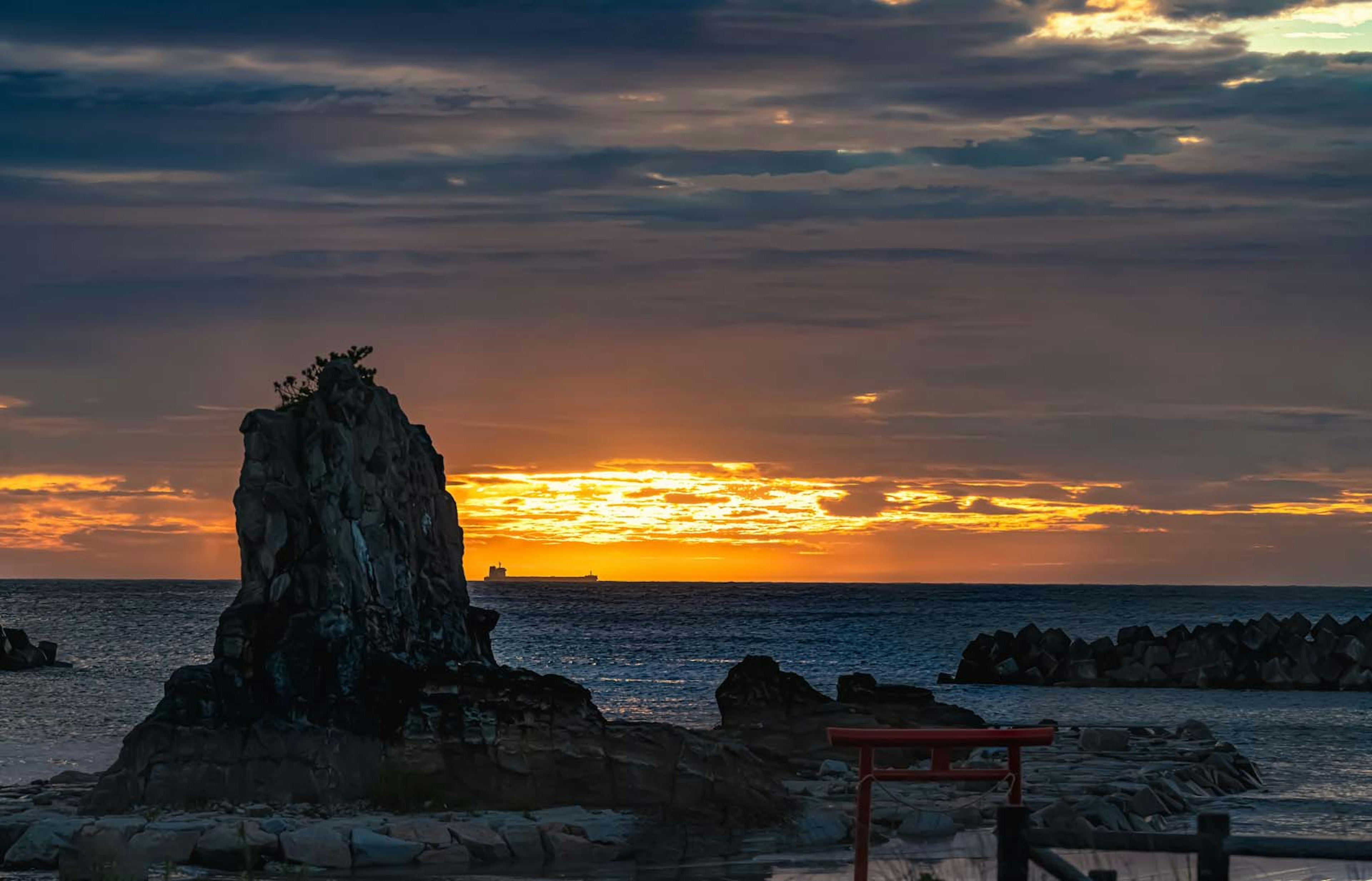 Batu pantai dengan matahari terbenam dan kapal di latar belakang