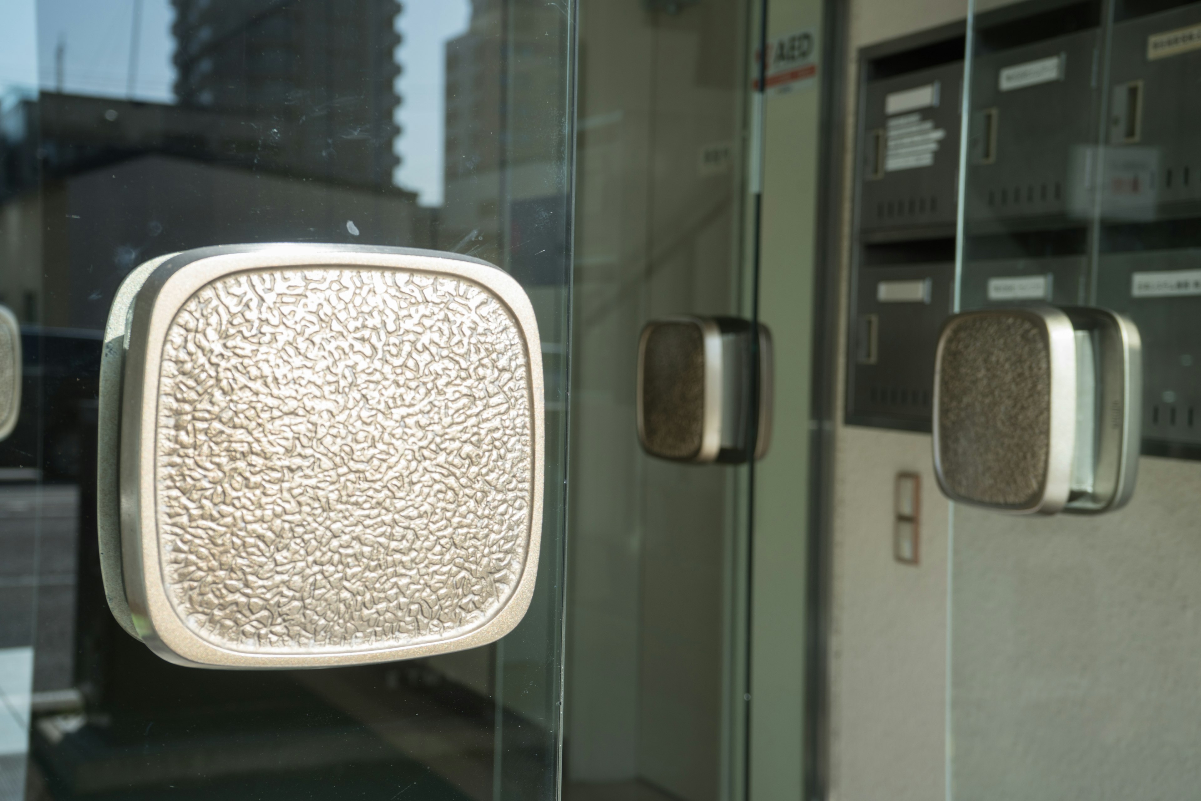 Metal door handles on glass door with reflections of surrounding buildings