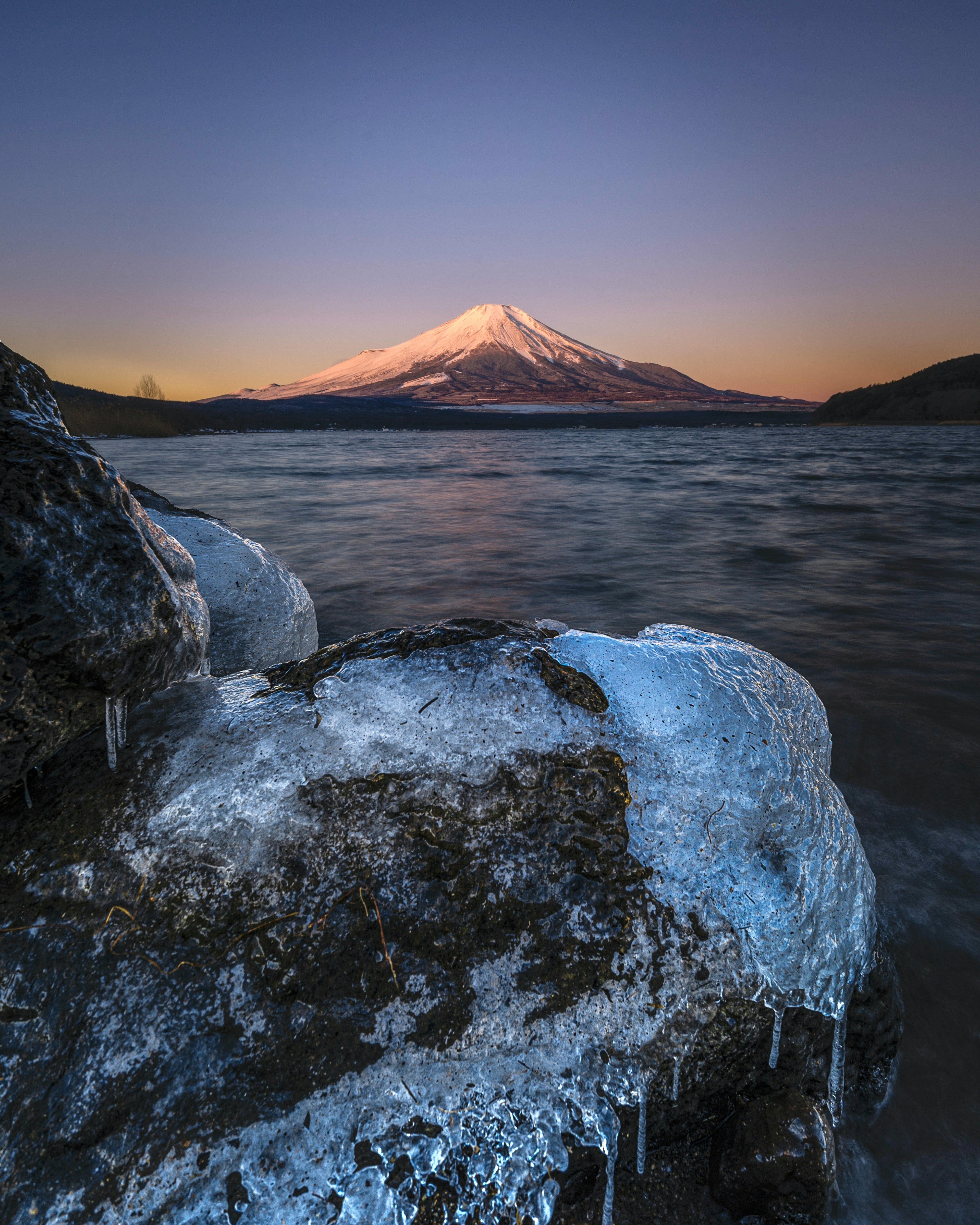 Scenic view of a snow-capped mountain with frozen rocks and water surface