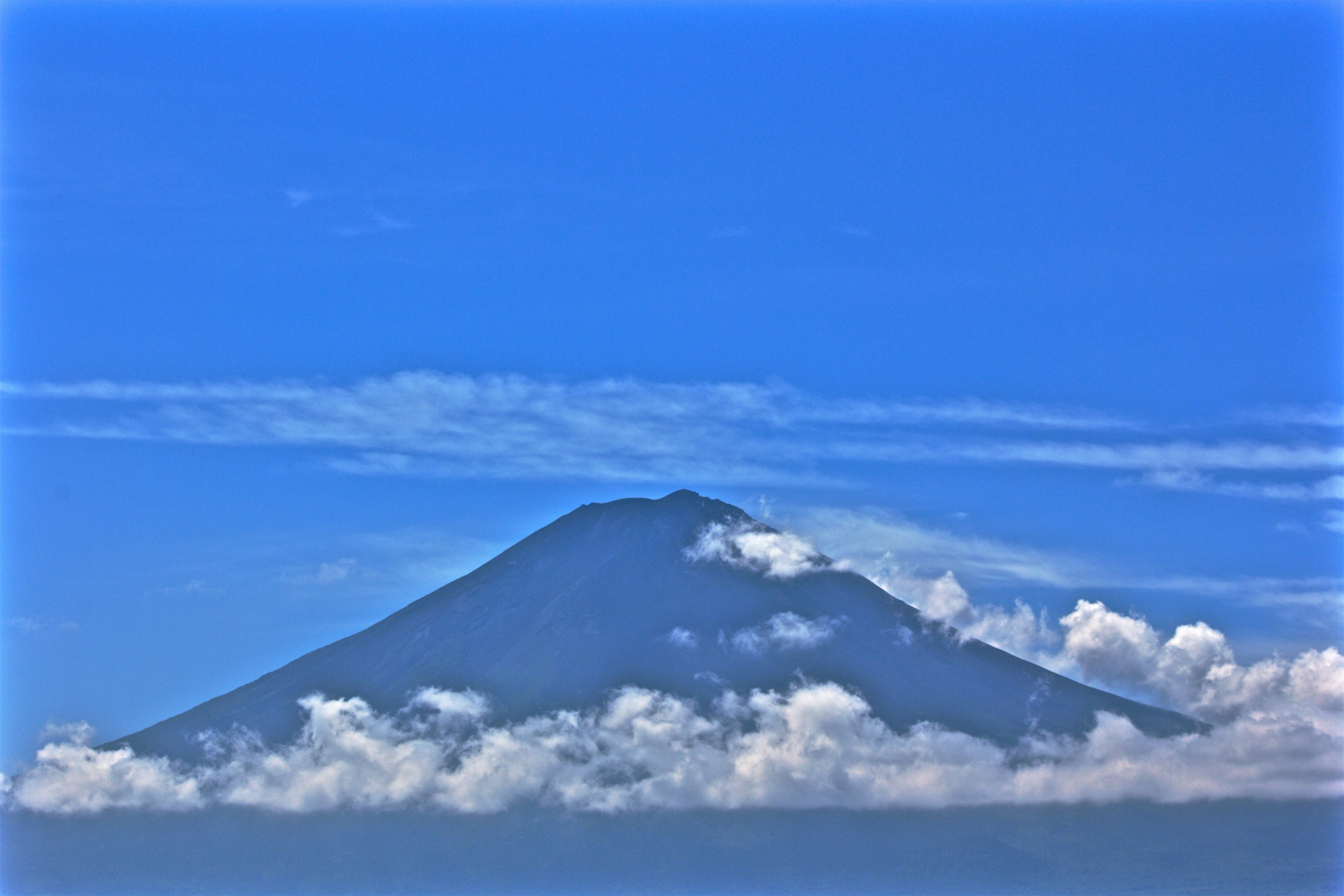 Pemandangan gunung megah di bawah langit biru dikelilingi awan