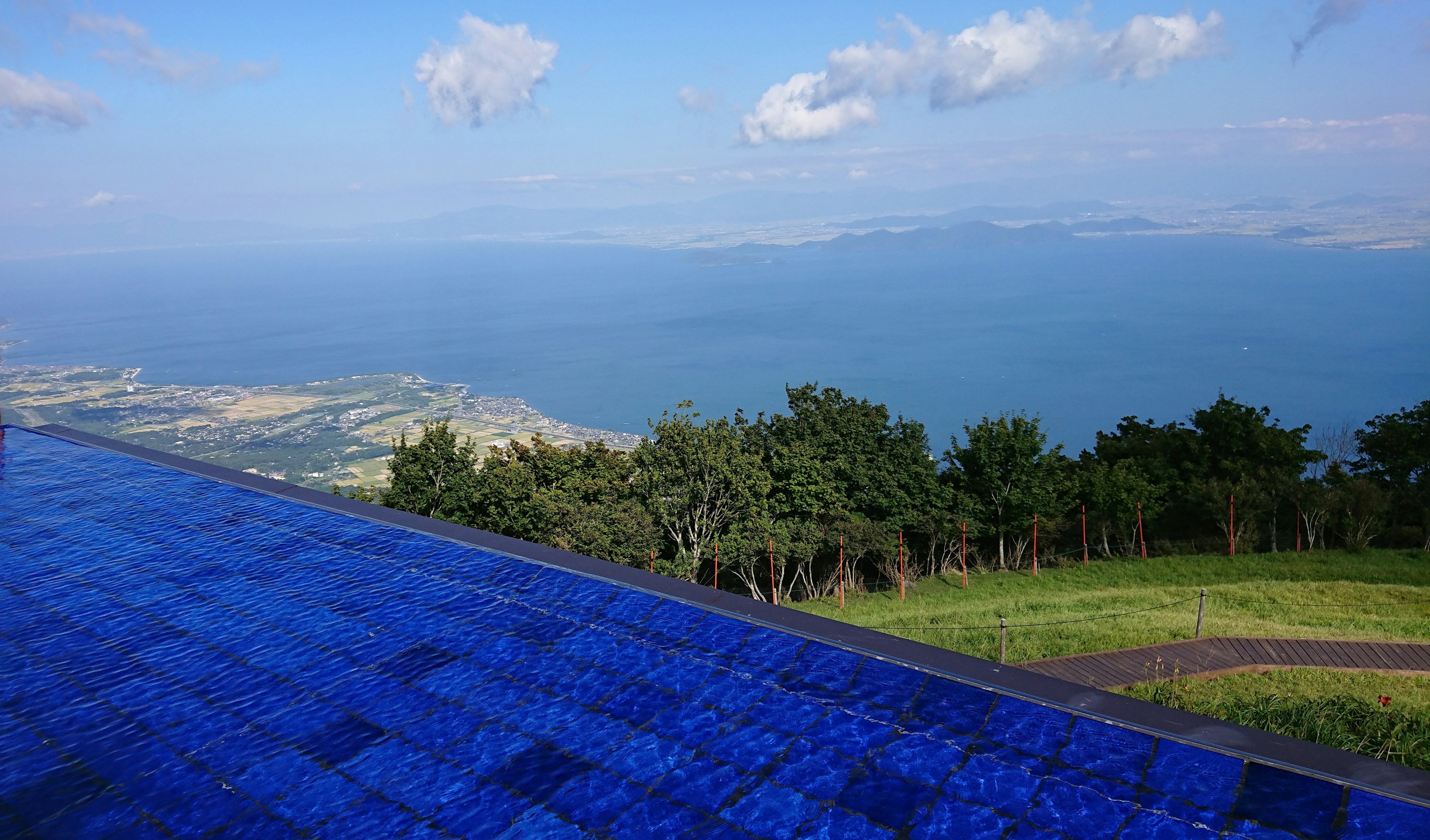 View of a blue pool edge overlooking green trees and water