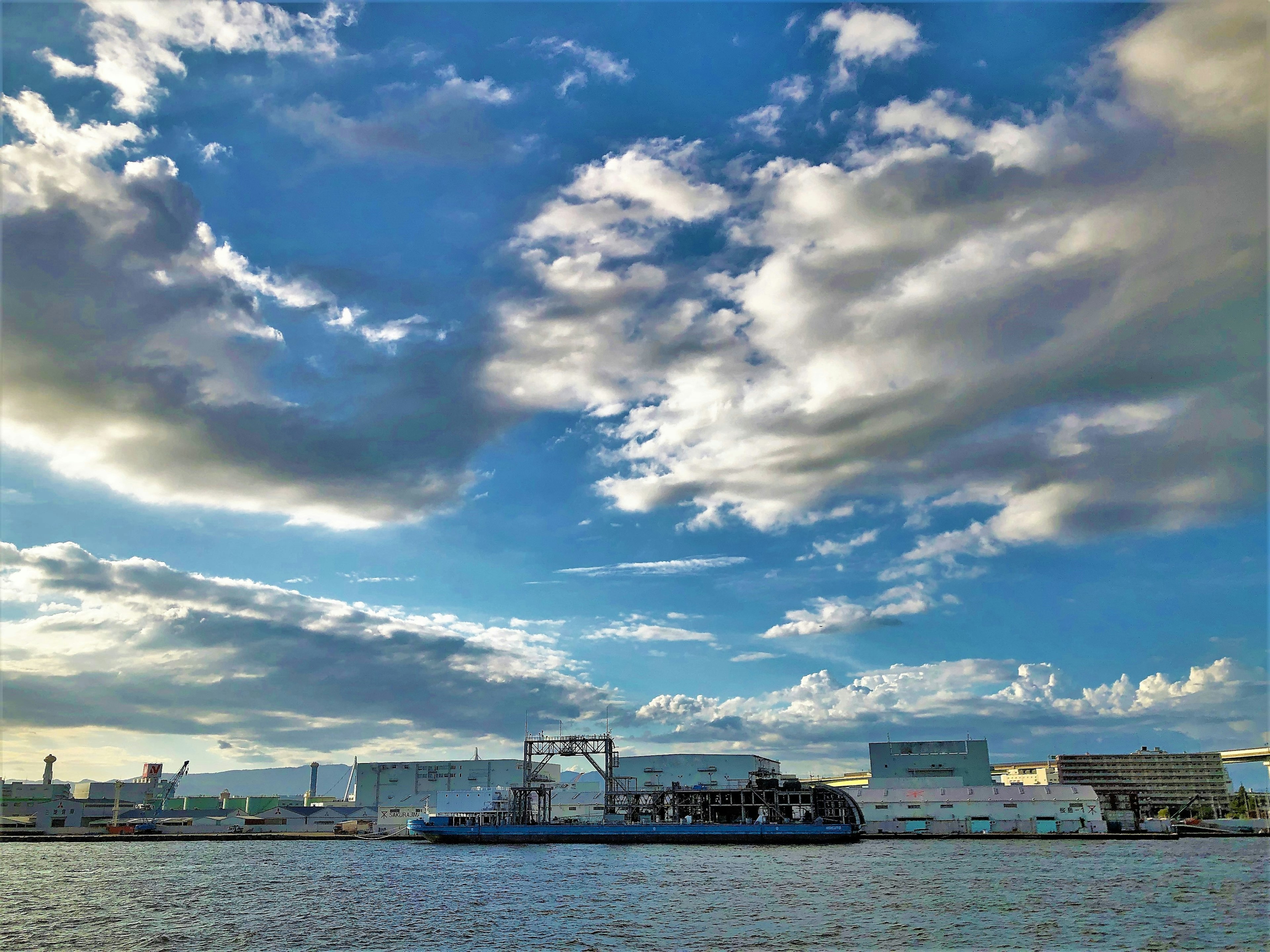 Hafenszene mit blauem Himmel und Wolken zeigt ein Schiff und Gebäude