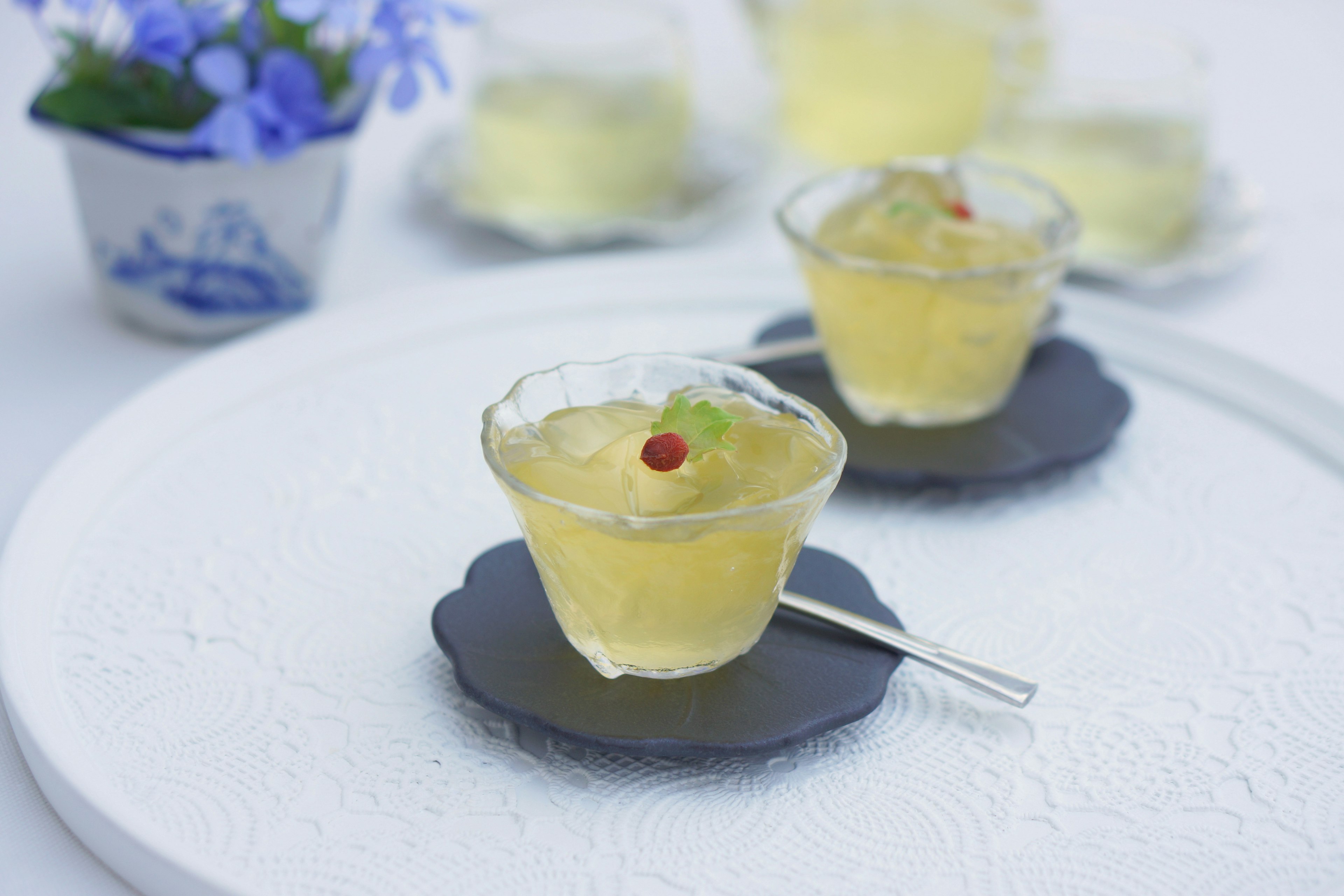 Dessert en gelée transparente servi sur une assiette noire avec un petit vase de fleurs bleues en arrière-plan