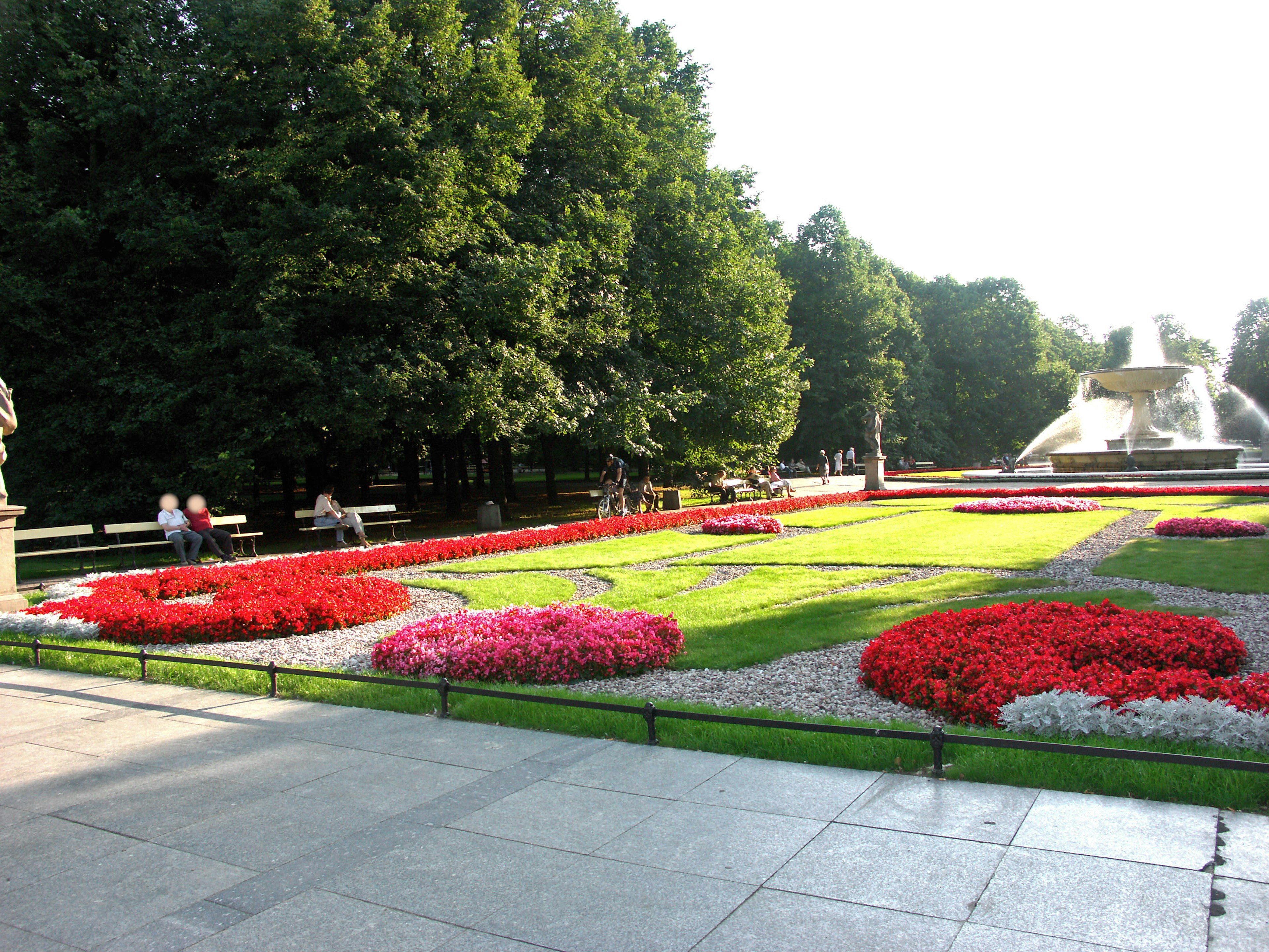 Flowerbed in a park surrounded by green trees with red and pink flowers