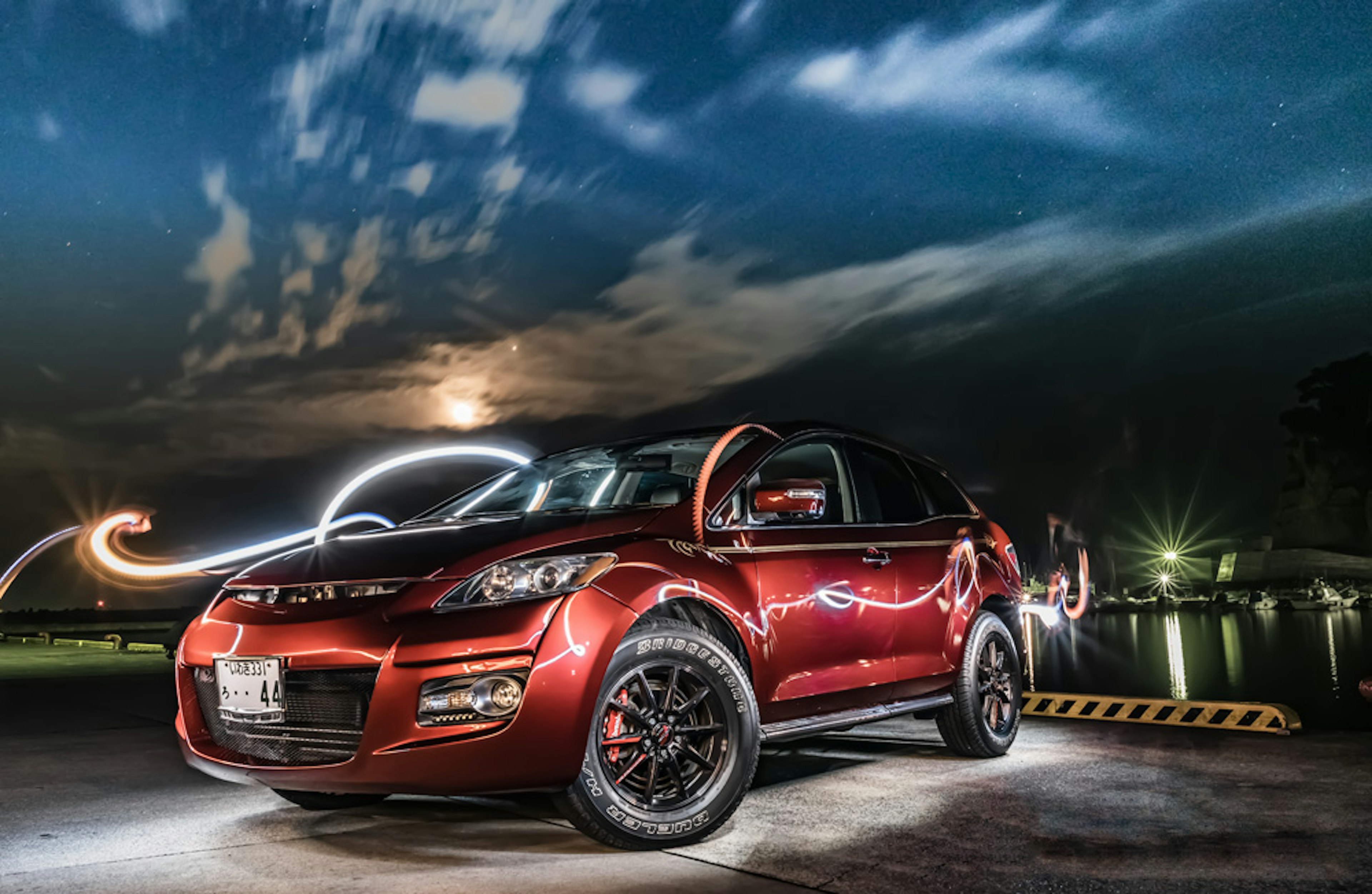 Red SUV parked at night under moonlight with light trails