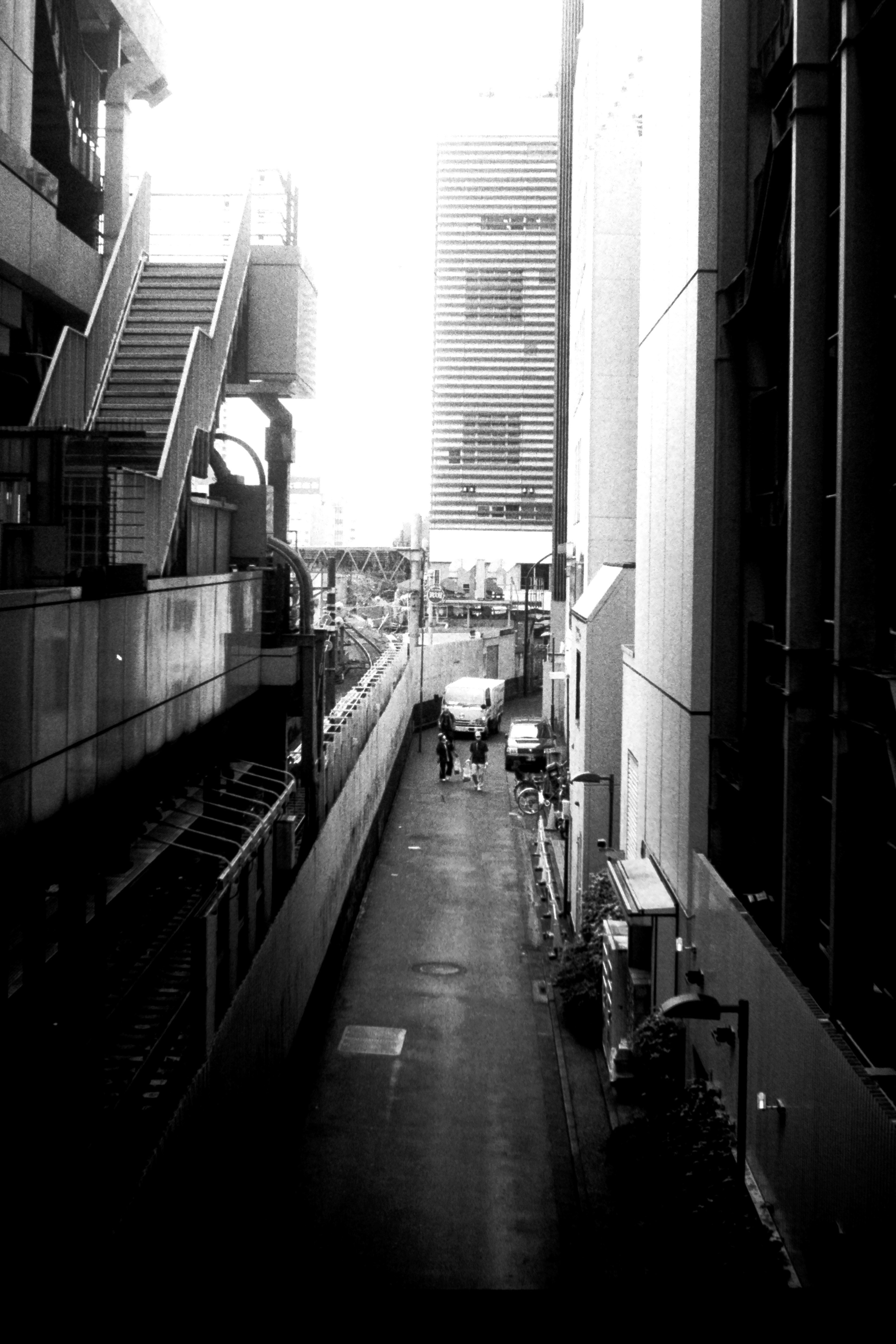 Allée urbaine en noir et blanc avec des bâtiments et des escaliers visibles