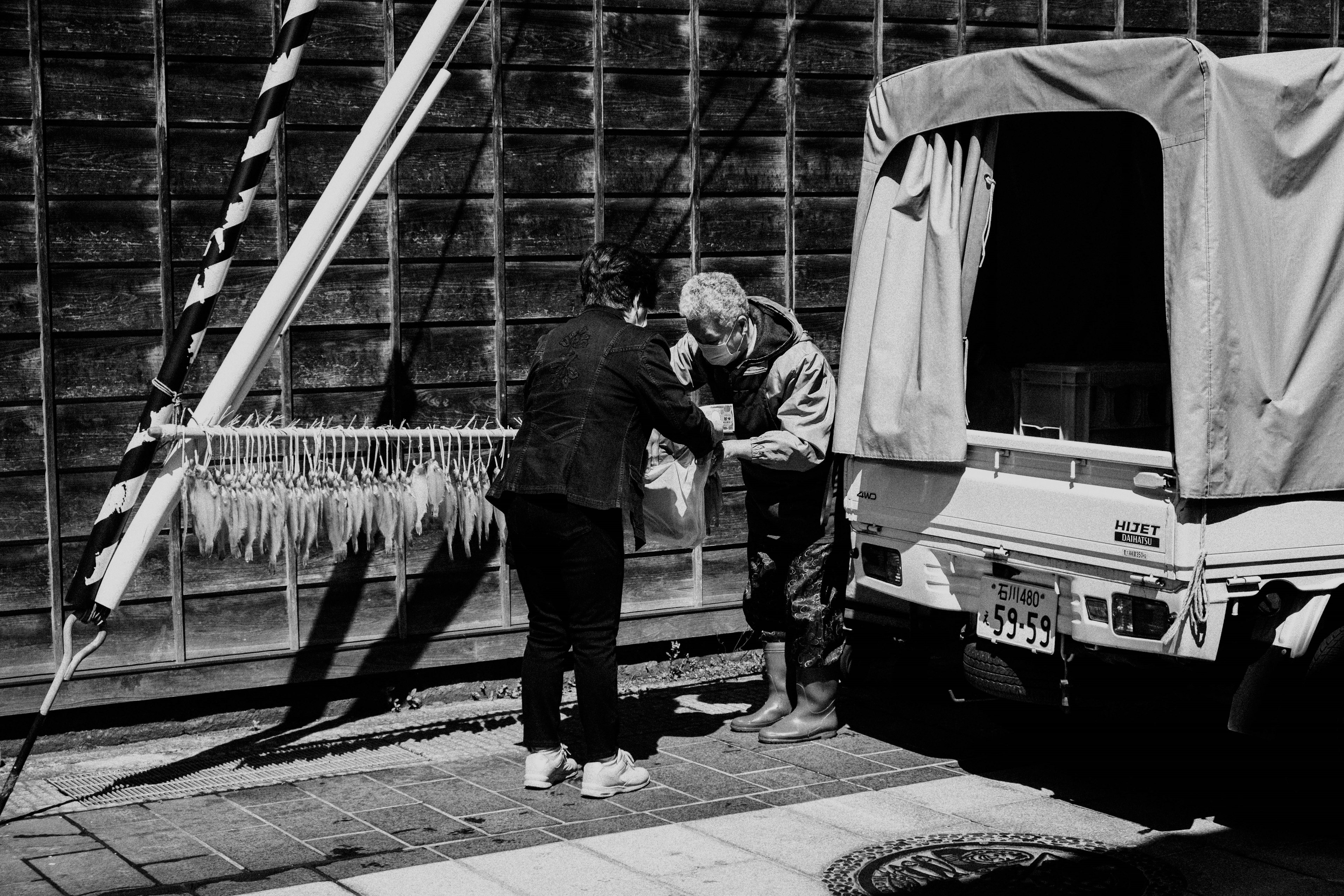 Dos personas intercambiando paquetes en una escena de calle en blanco y negro con la silueta de un vehículo