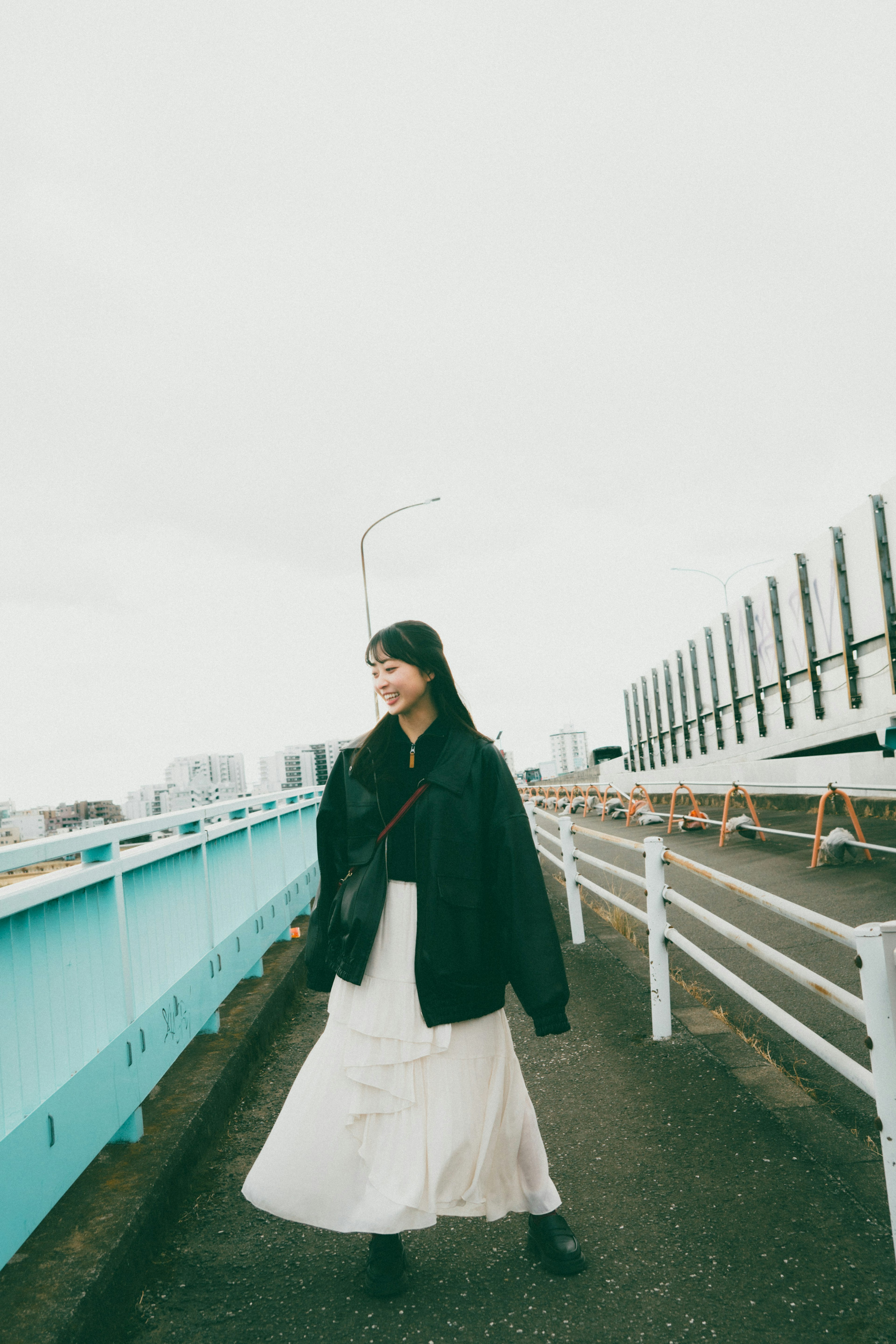 Woman wearing a black jacket and white skirt walking on a bridge