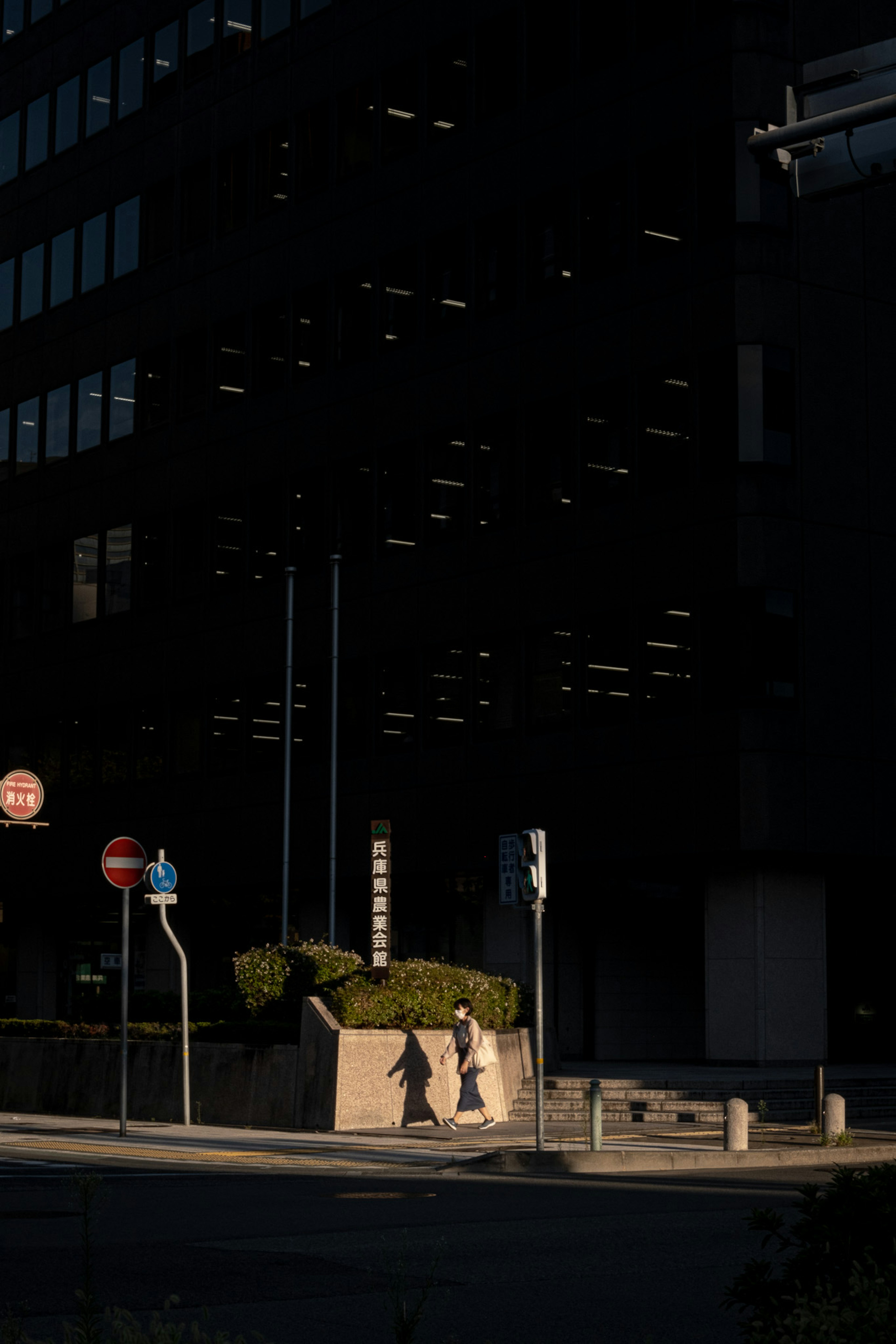 People walking in front of a dark building with streetlights