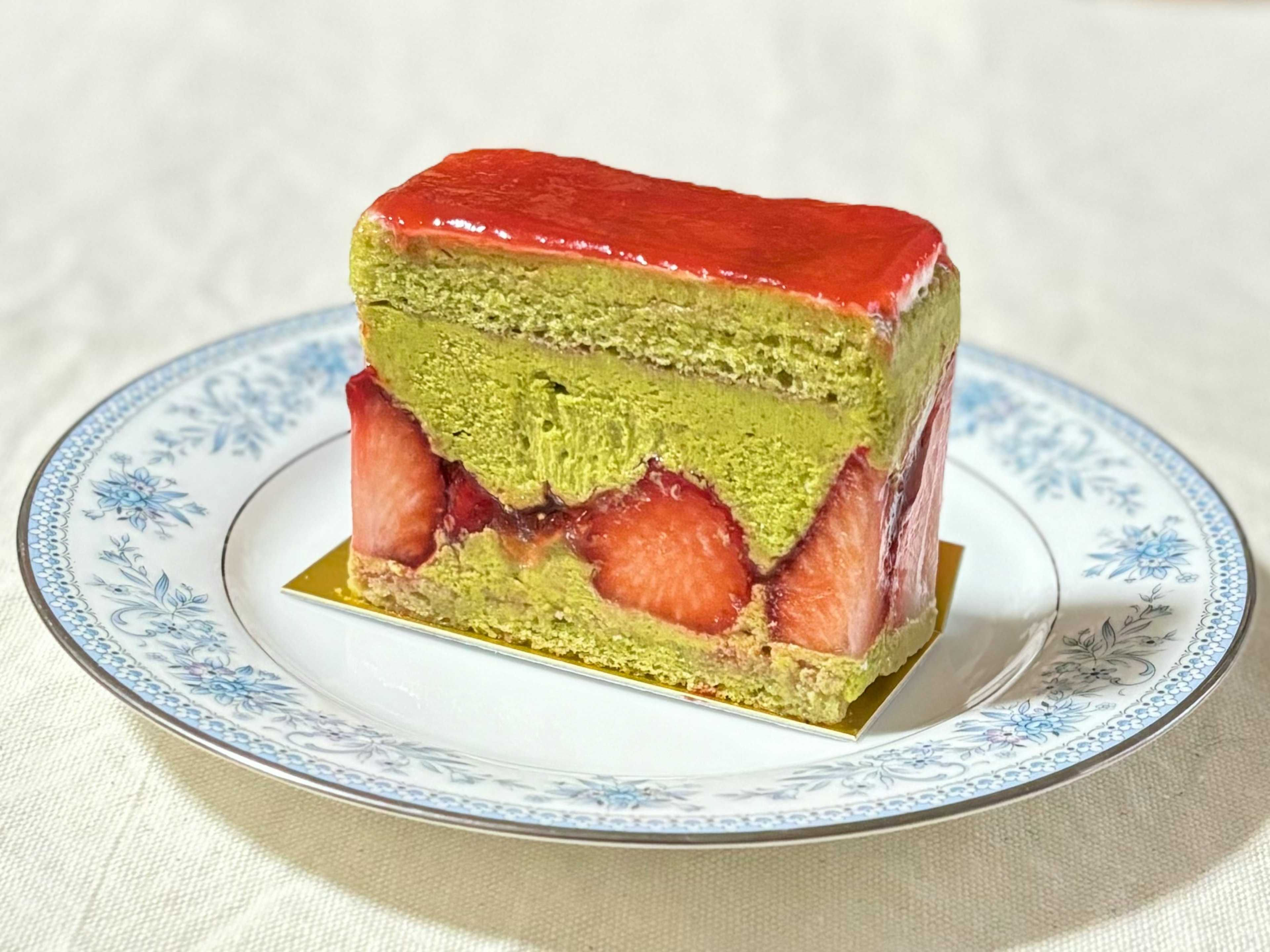 A beautiful layered cake with matcha and strawberries served on a blue floral plate