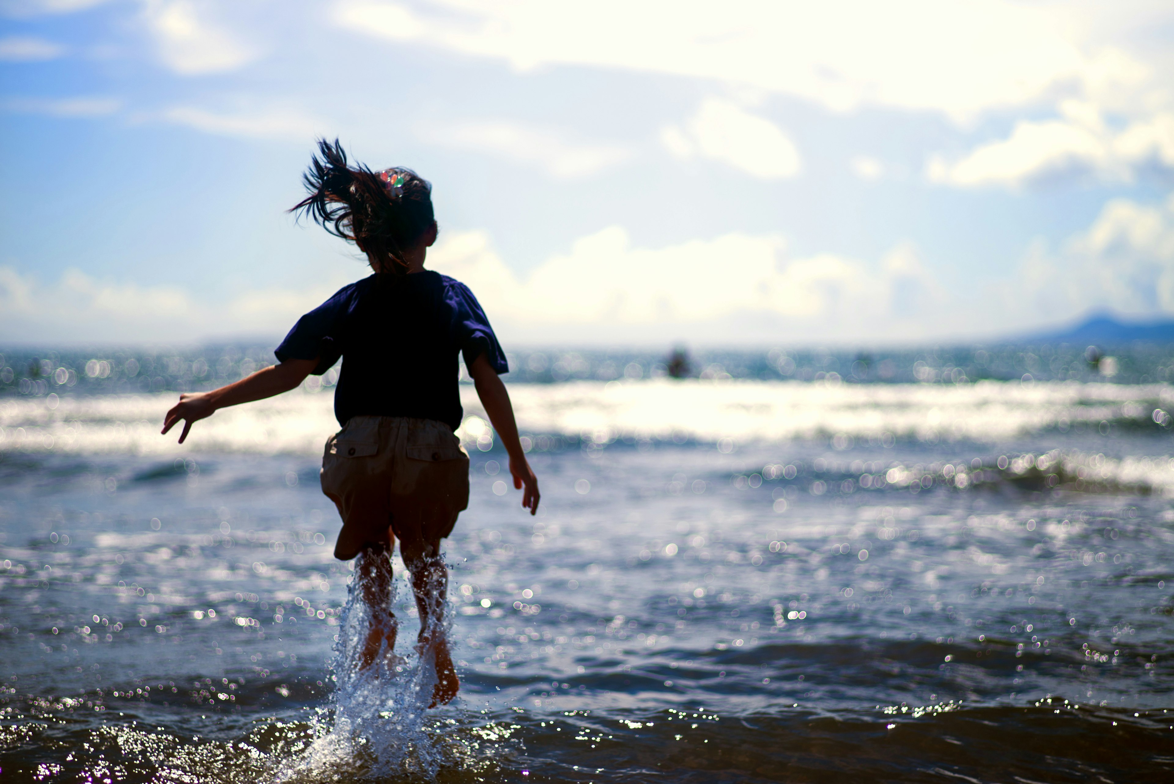 Child splashing in the ocean water with a bright sky background