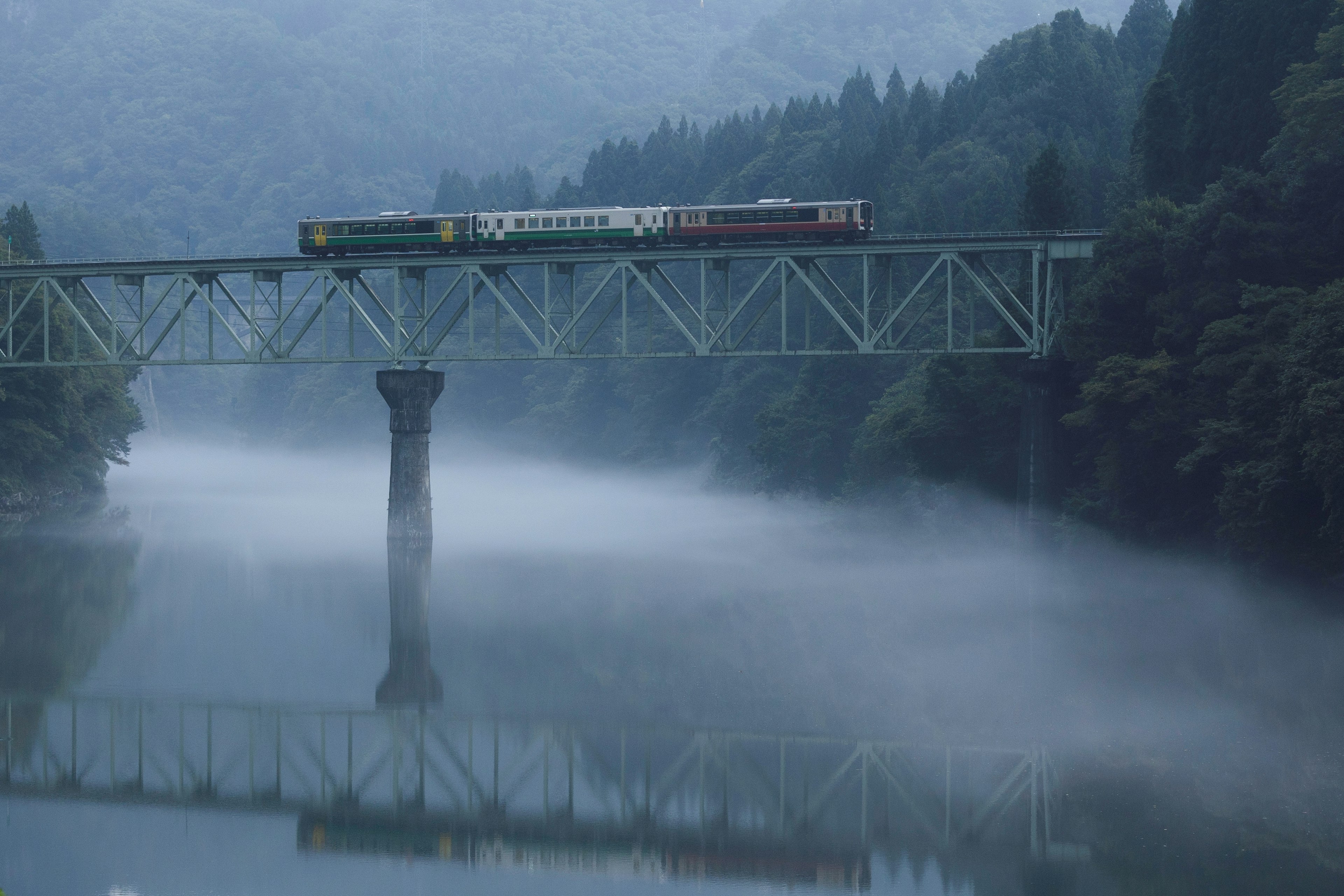 霧に包まれた川を渡る列車と鉄橋の風景