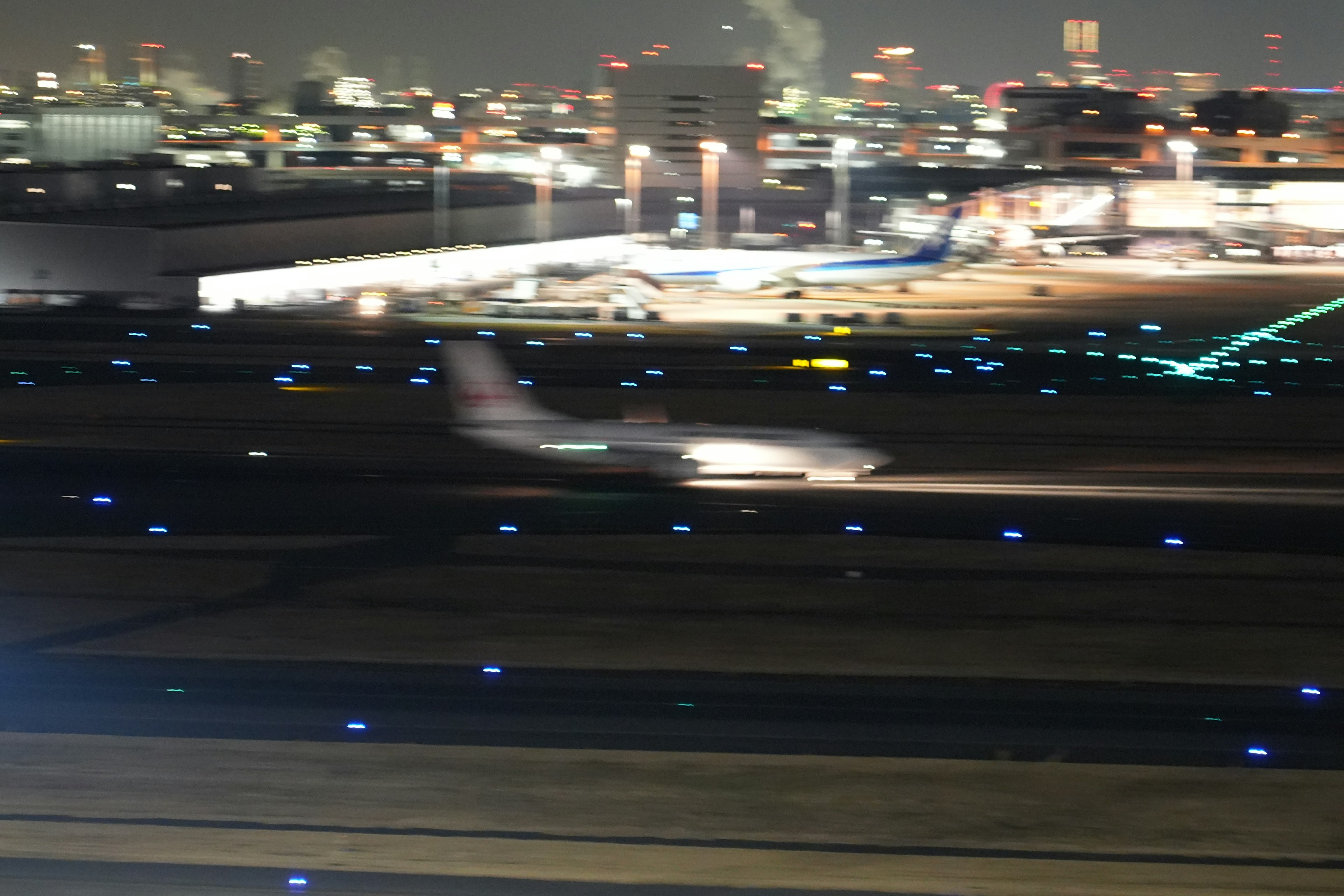 Airplane landing at night with illuminated airport background