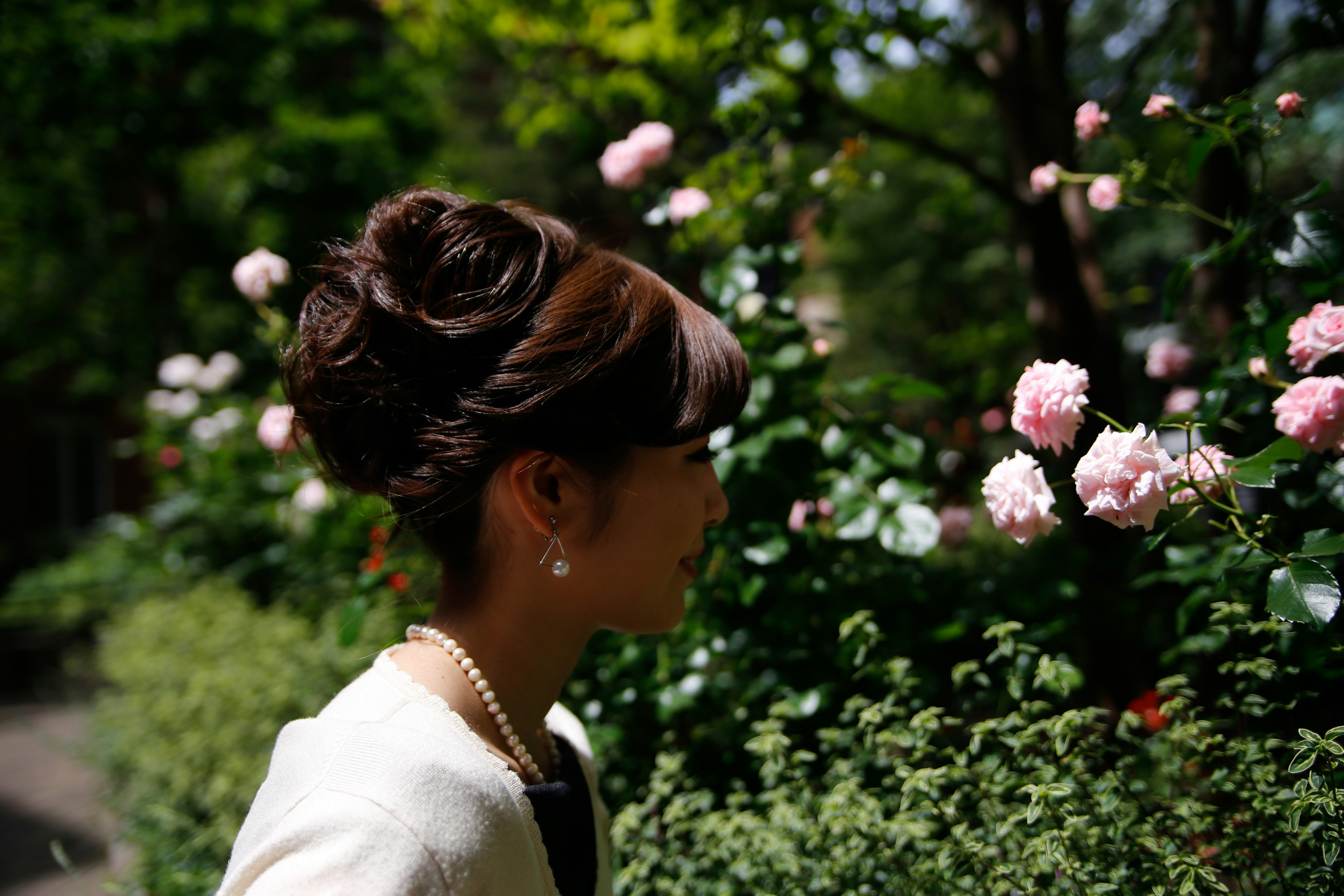 Una donna che guarda rose in fiore con un'acconciatura elegante e una giacca bianca