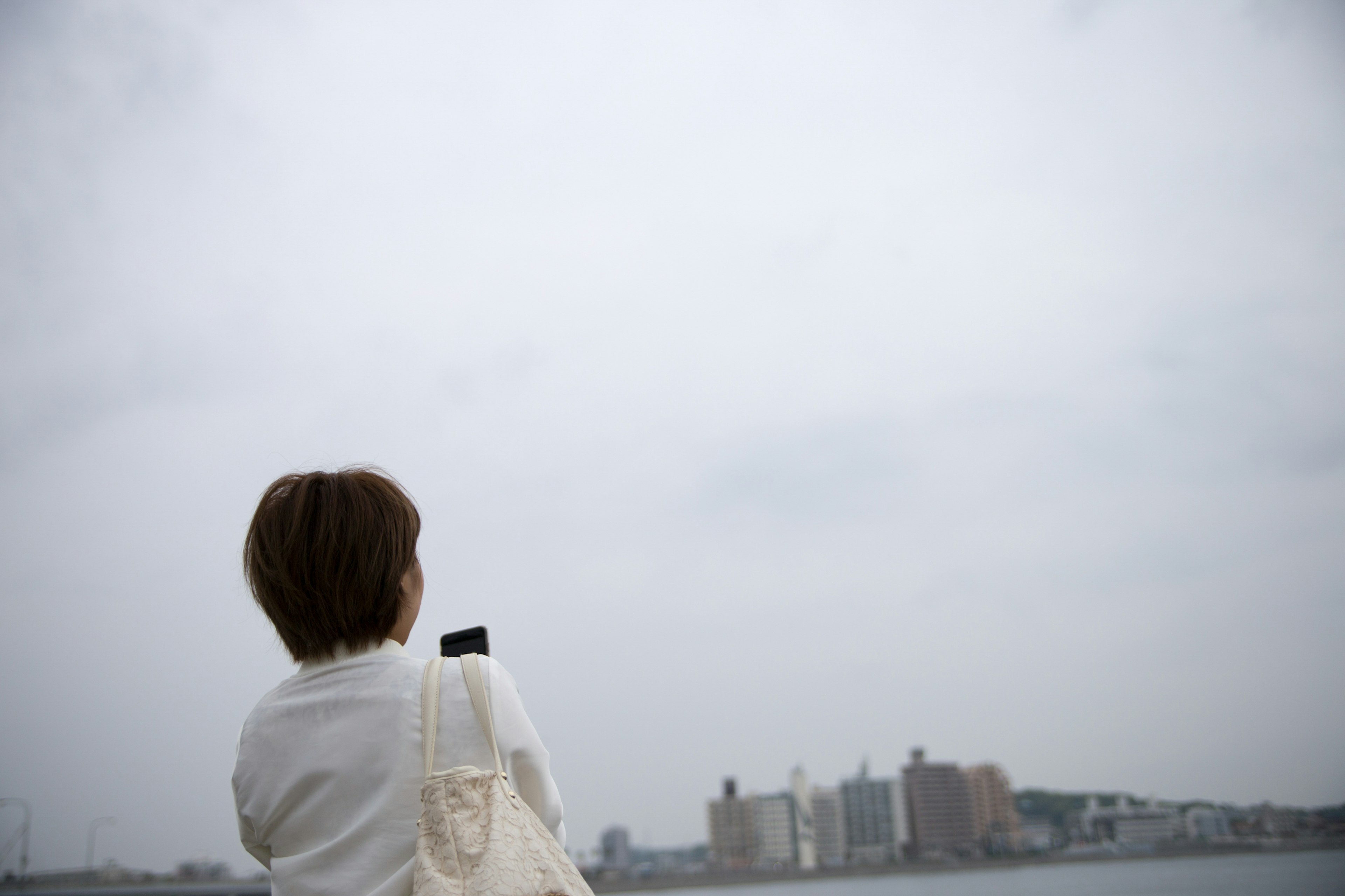 曇り空の下、背を向けた女性が都市の景色を眺めている