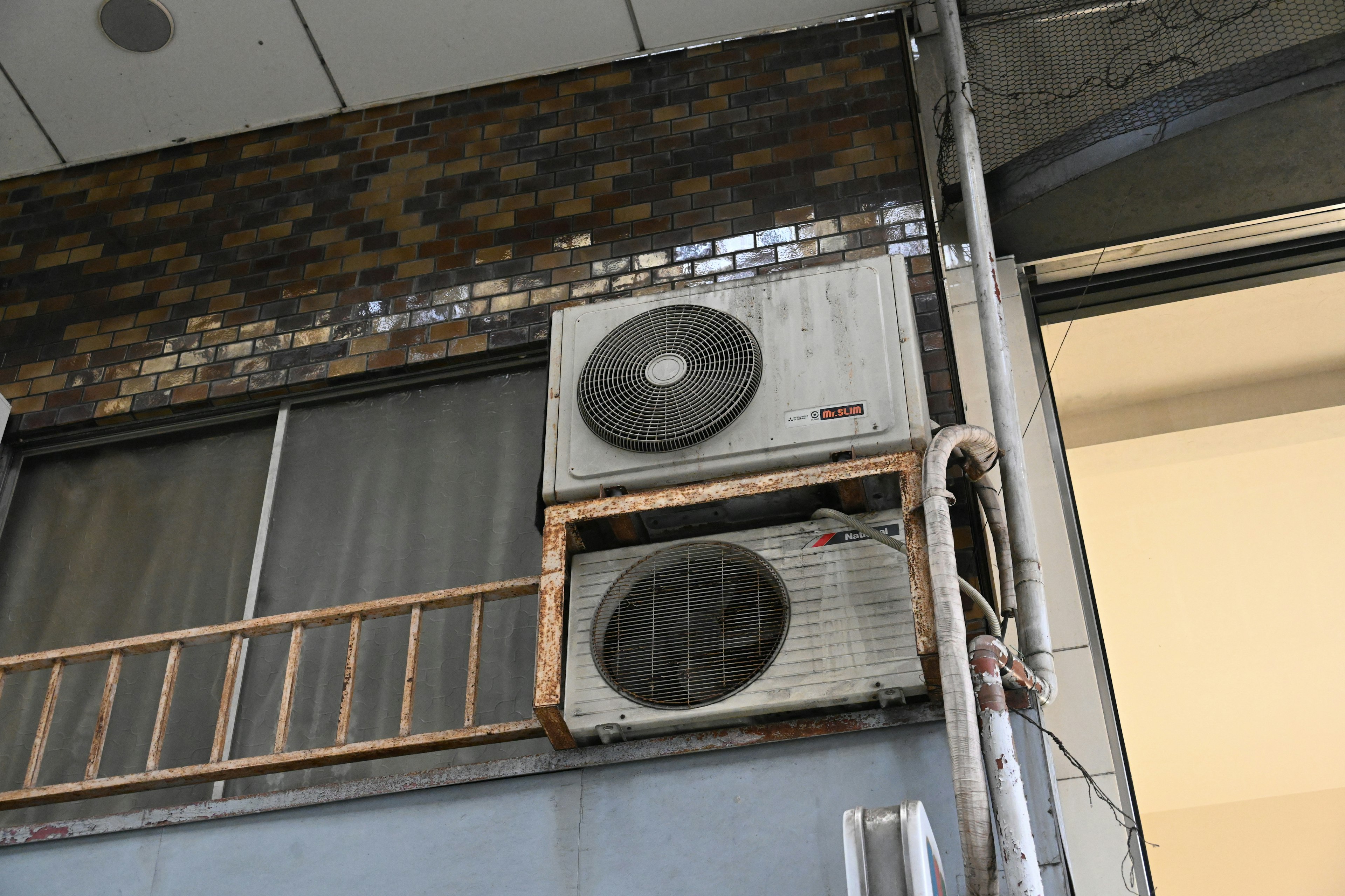 Two air conditioning units mounted on the exterior wall of an old building