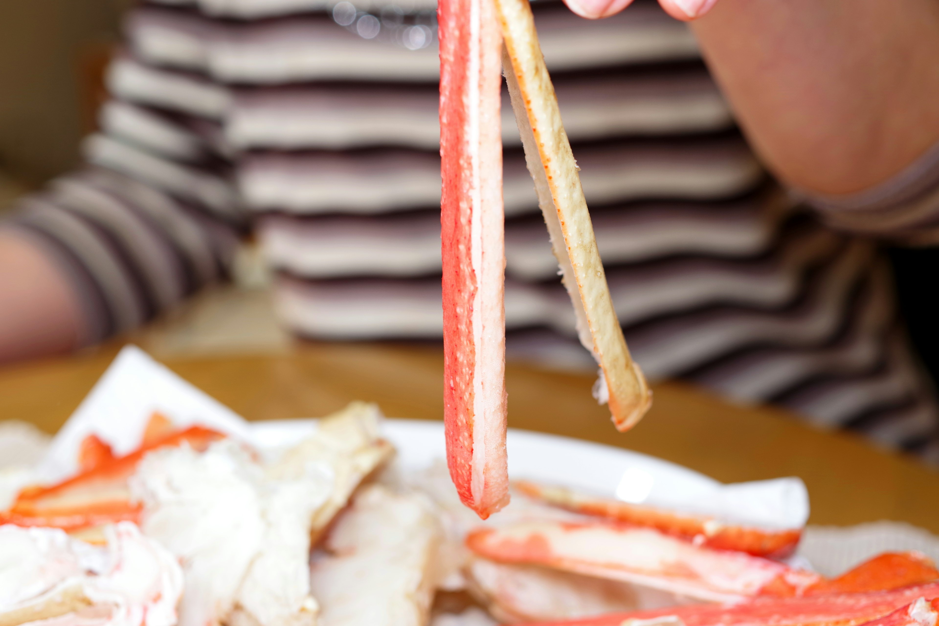 Une personne en chemise rayée tenant des pattes de crabe avec des baguettes