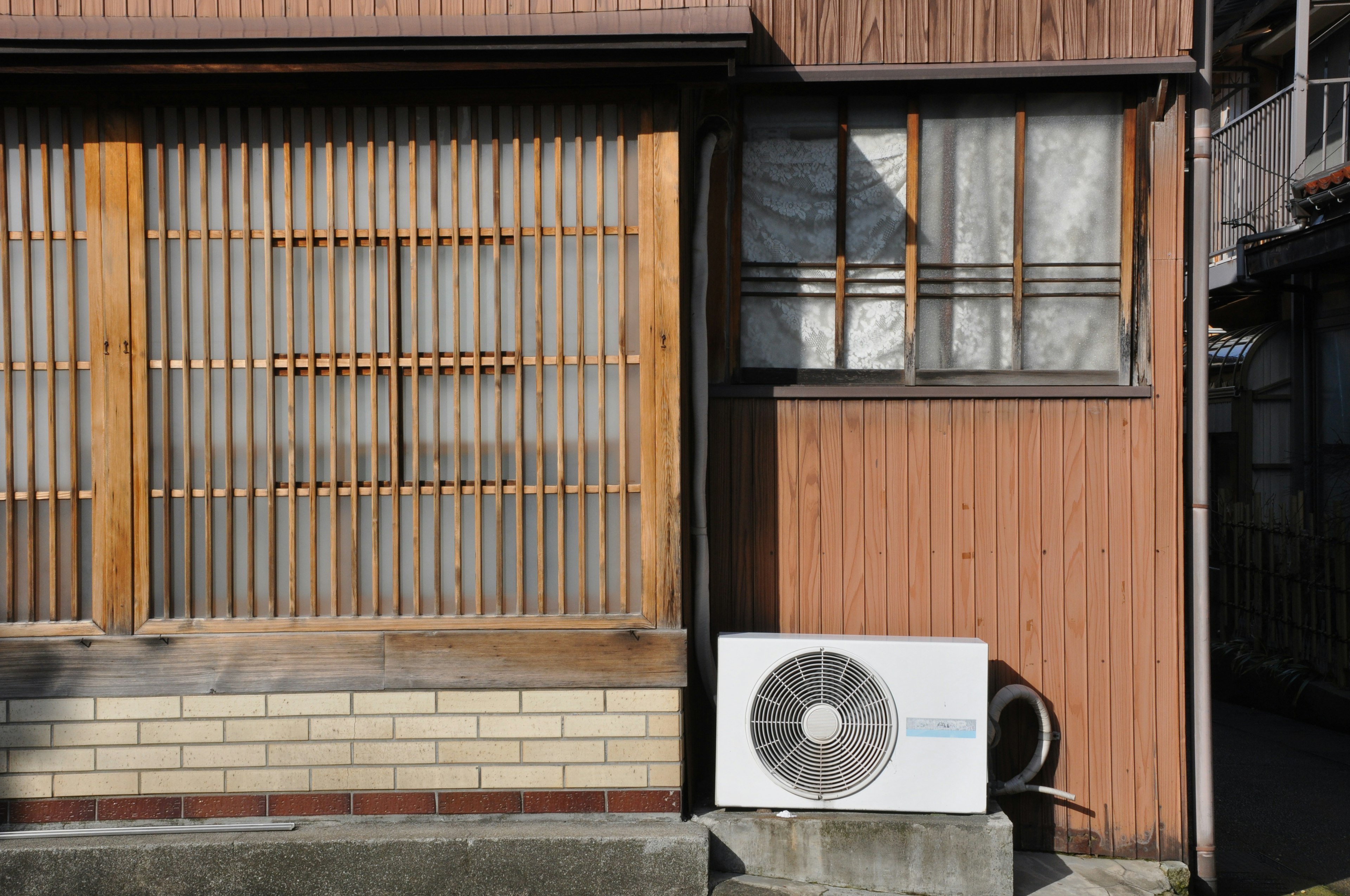 Exterior de una casa japonesa con ventanas de rejilla de madera y unidad de aire acondicionado