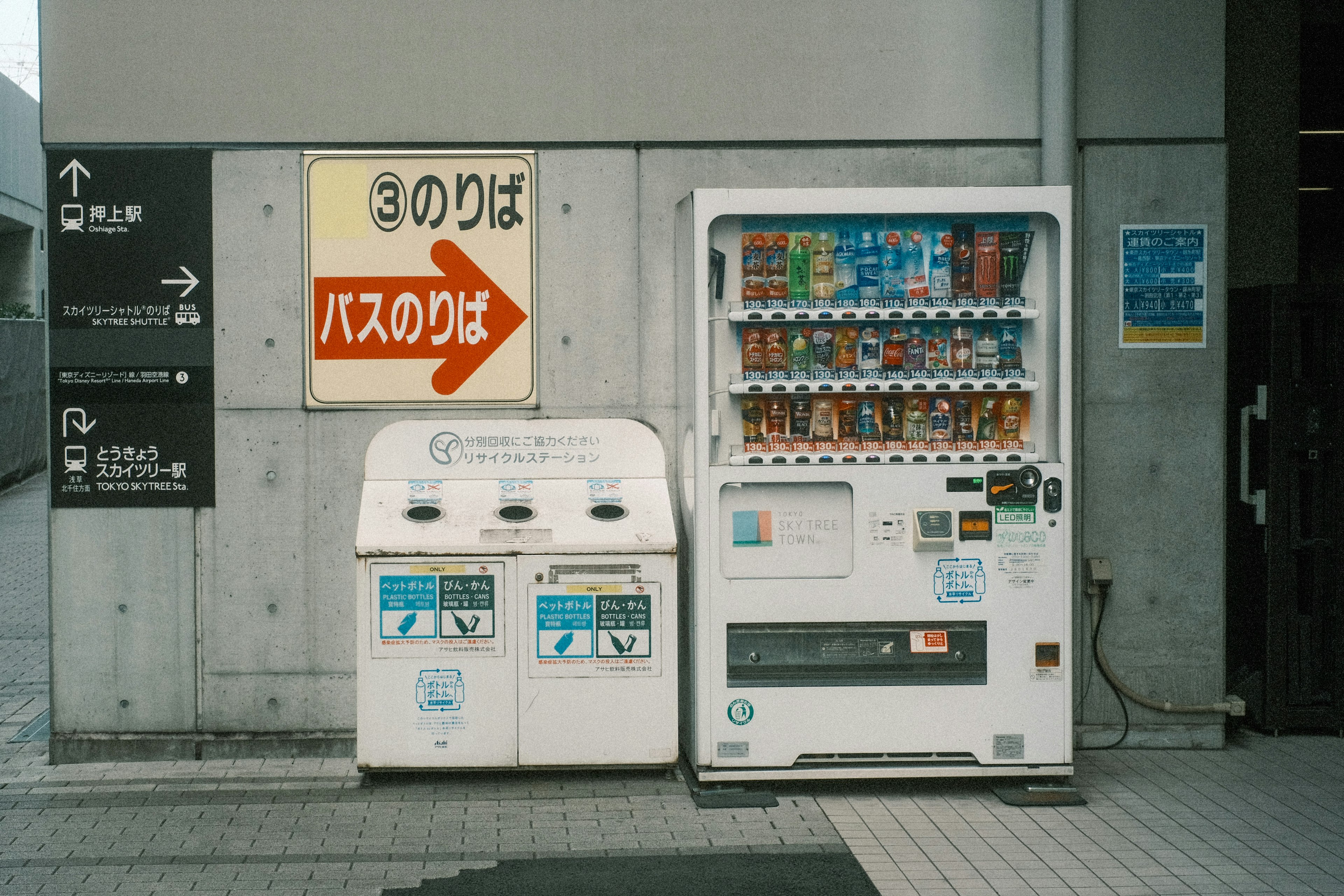 A vending machine next to two trash bins with a bus stop sign