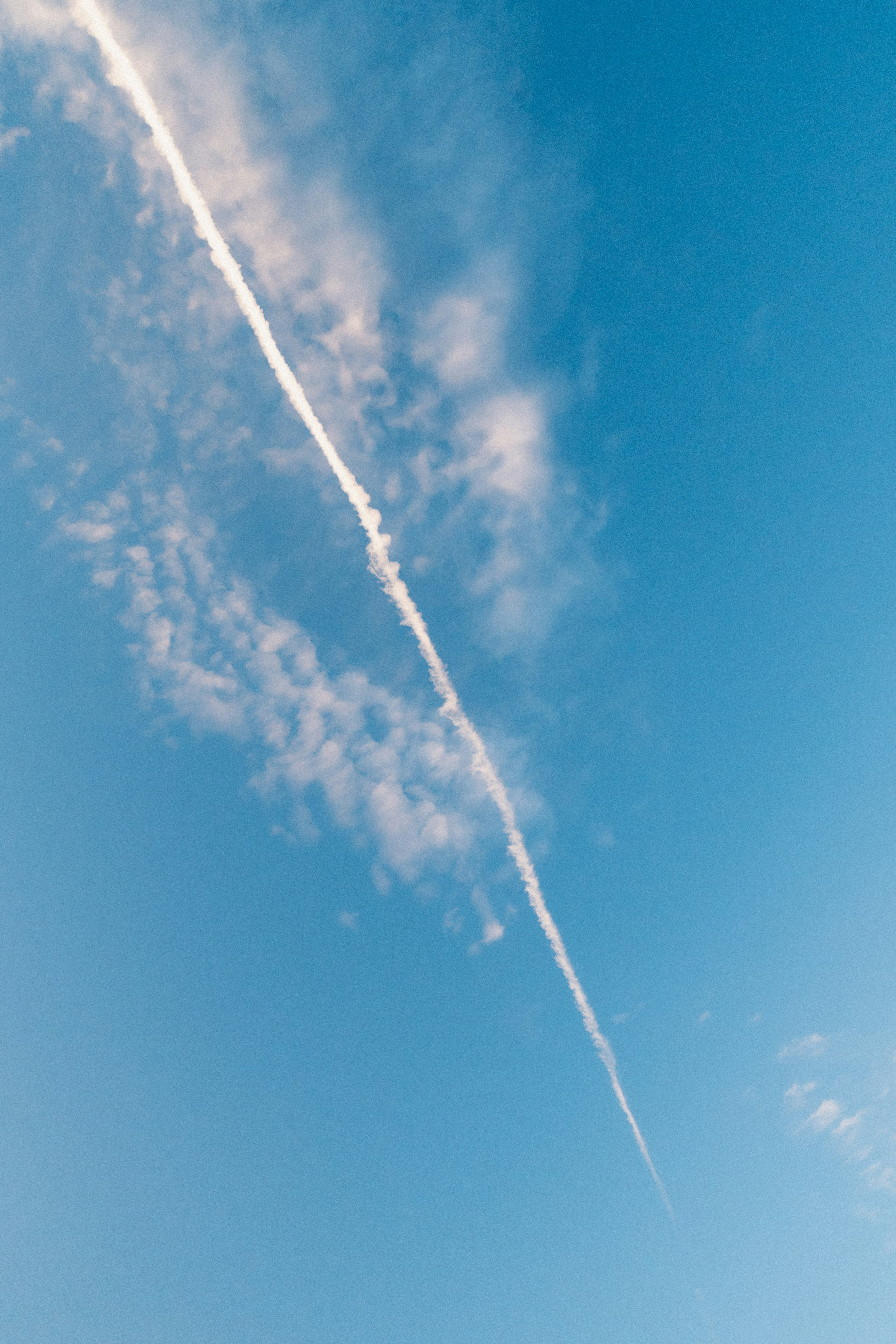 青空に白い飛行機雲が伸びる様子