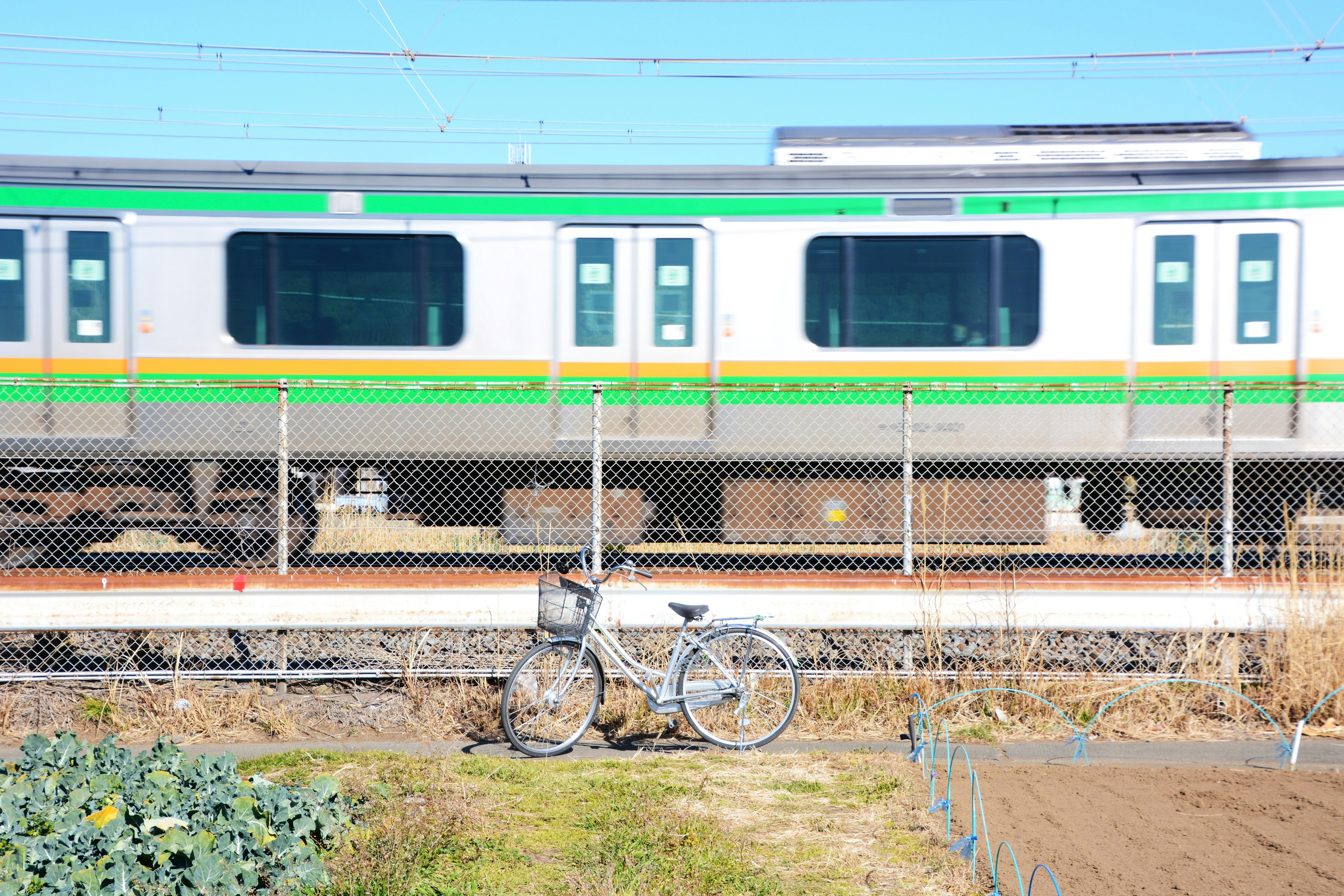 A green and silver train passing by with a bicycle parked nearby