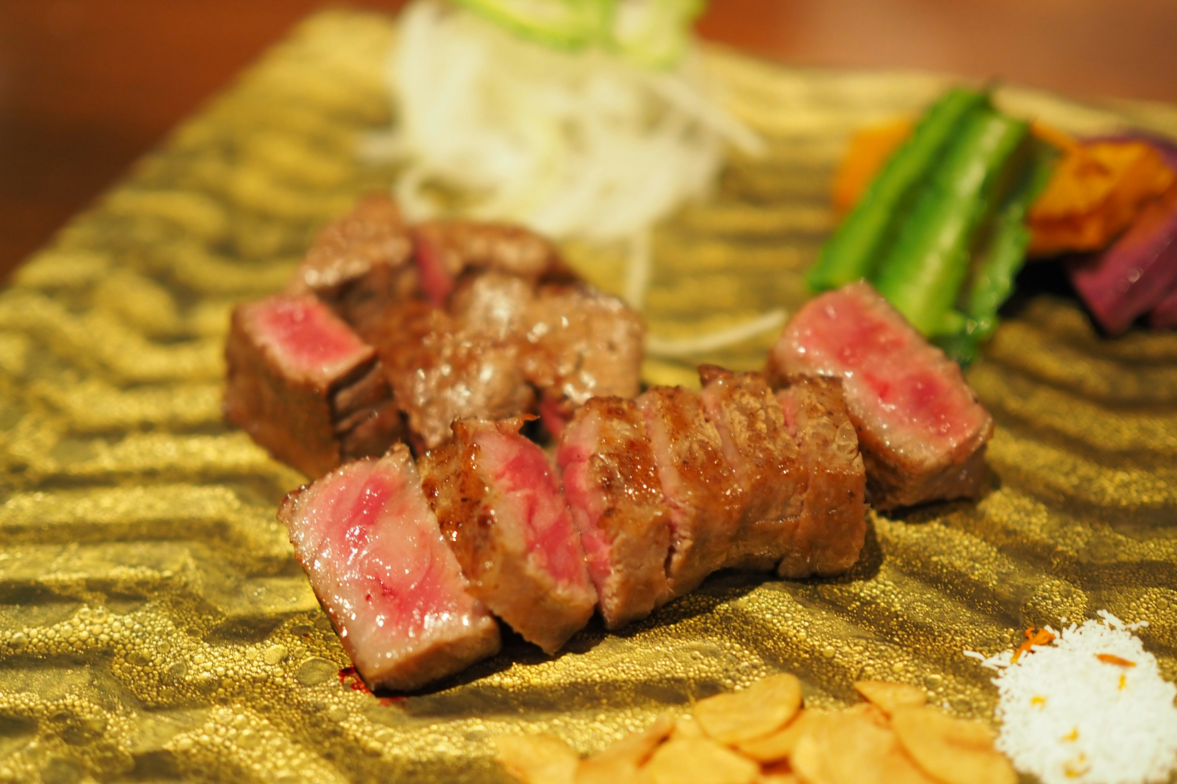 Sliced steak with a pink center on a decorative plate surrounded by colorful vegetables