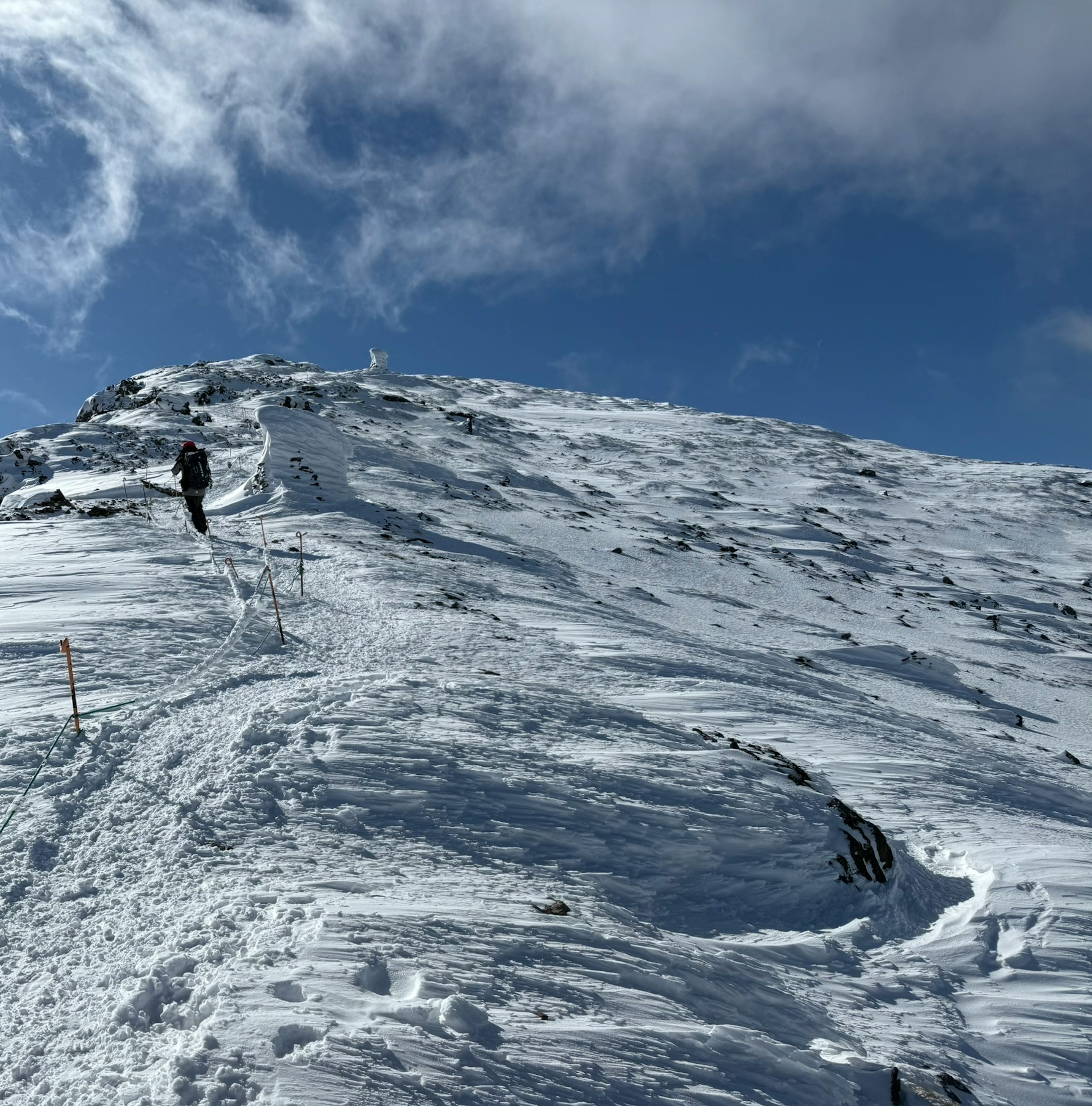 Wanderer, der einen schneebedeckten Berghang unter einem blauen Himmel erklimmt