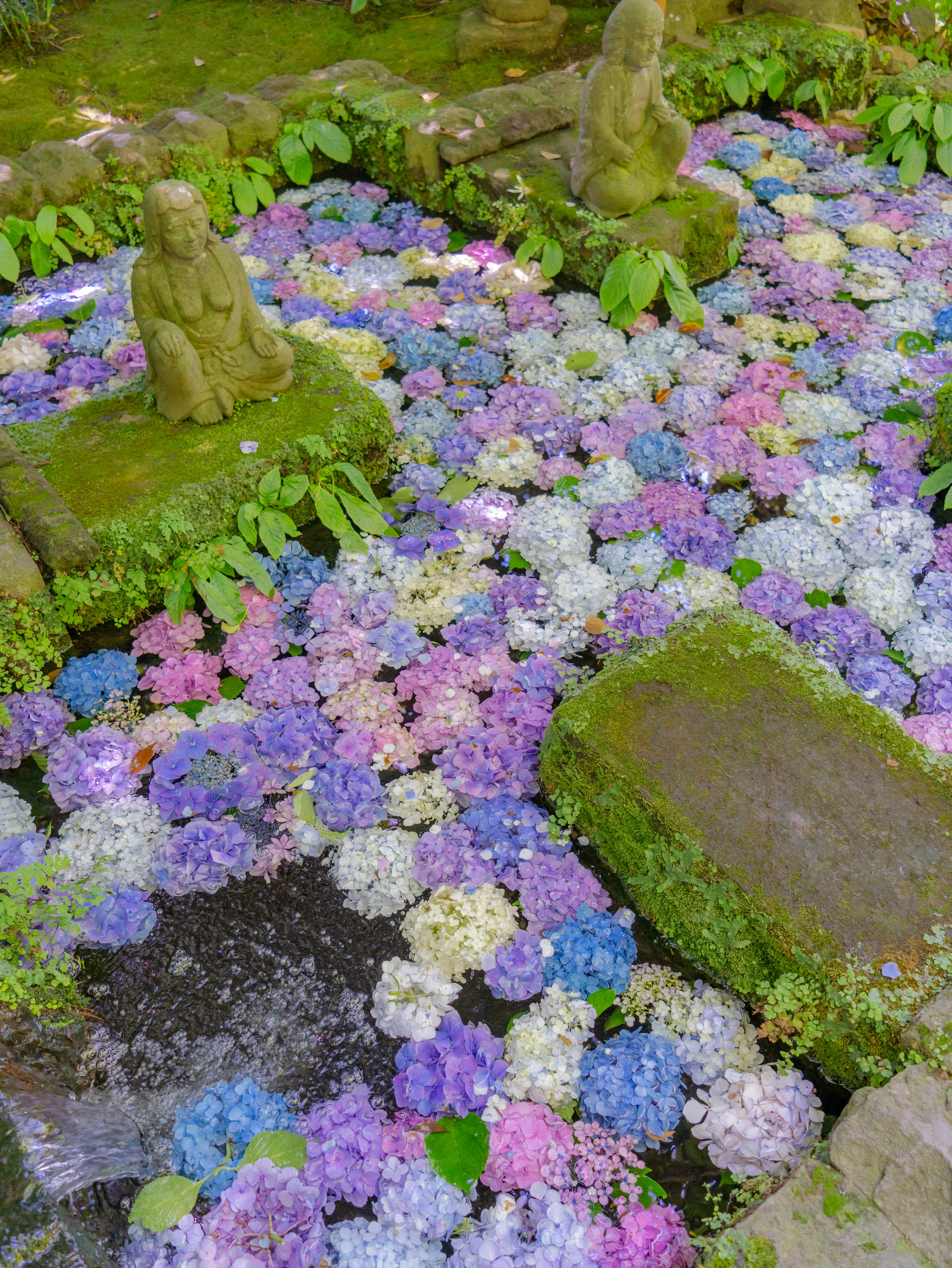 Un giardino pieno di fiori colorati che circondano statue di pietra coperte di muschio