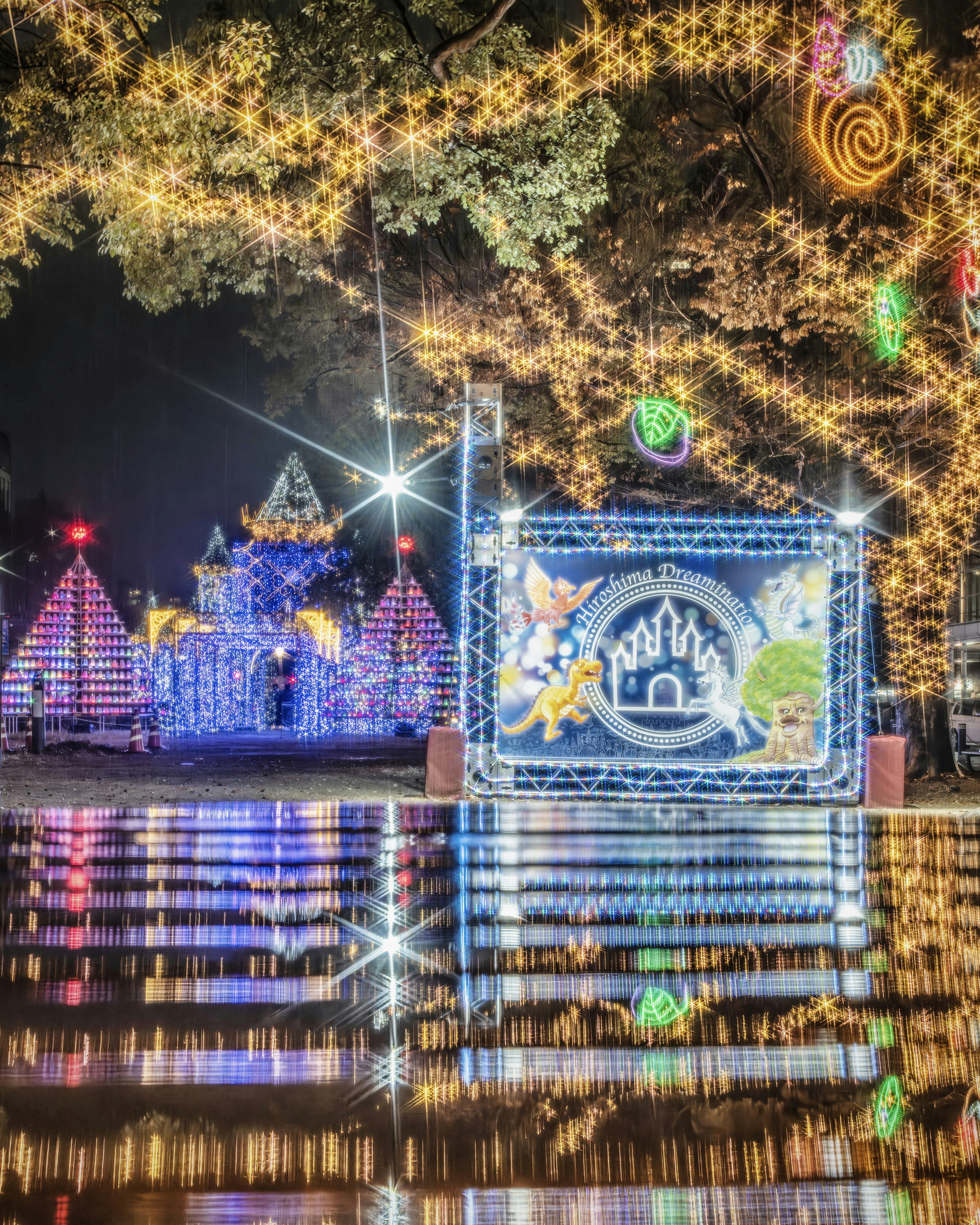 A festive display of Christmas lights in a park at night with reflections on the water