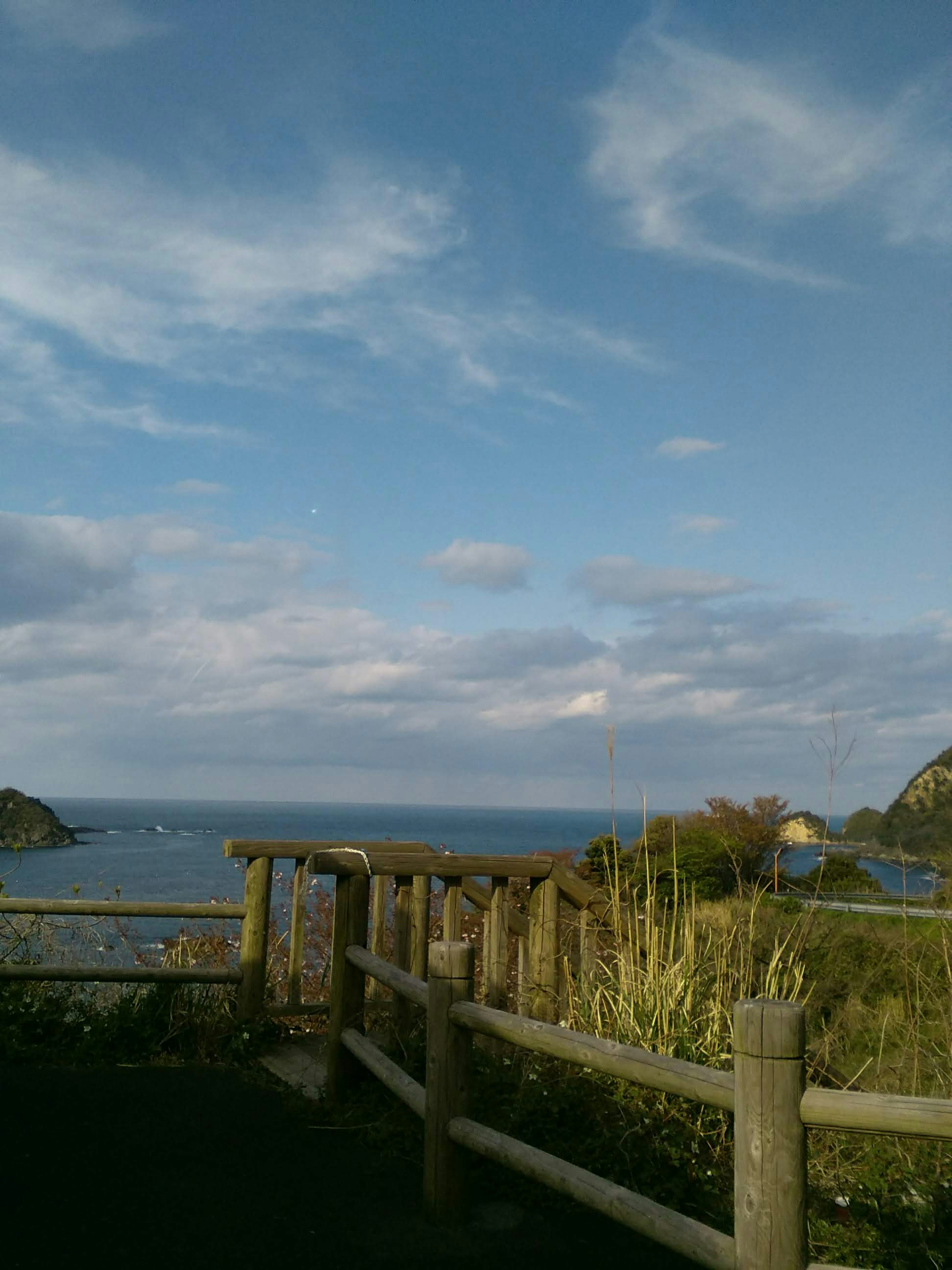 Vista escénica del océano y el cielo con una cerca de madera y vegetación