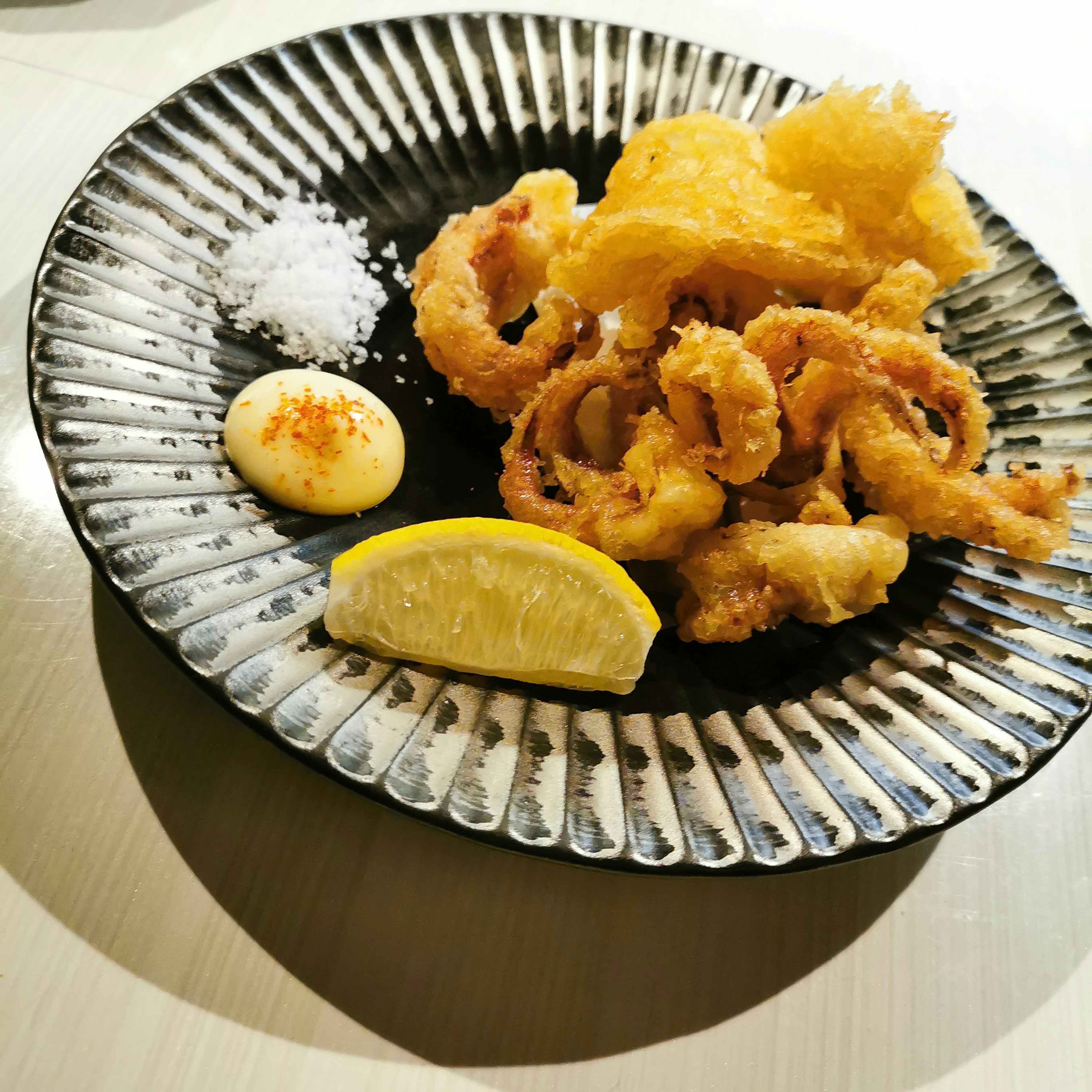 Fried calamari rings served on a black plate with lemon and sauce