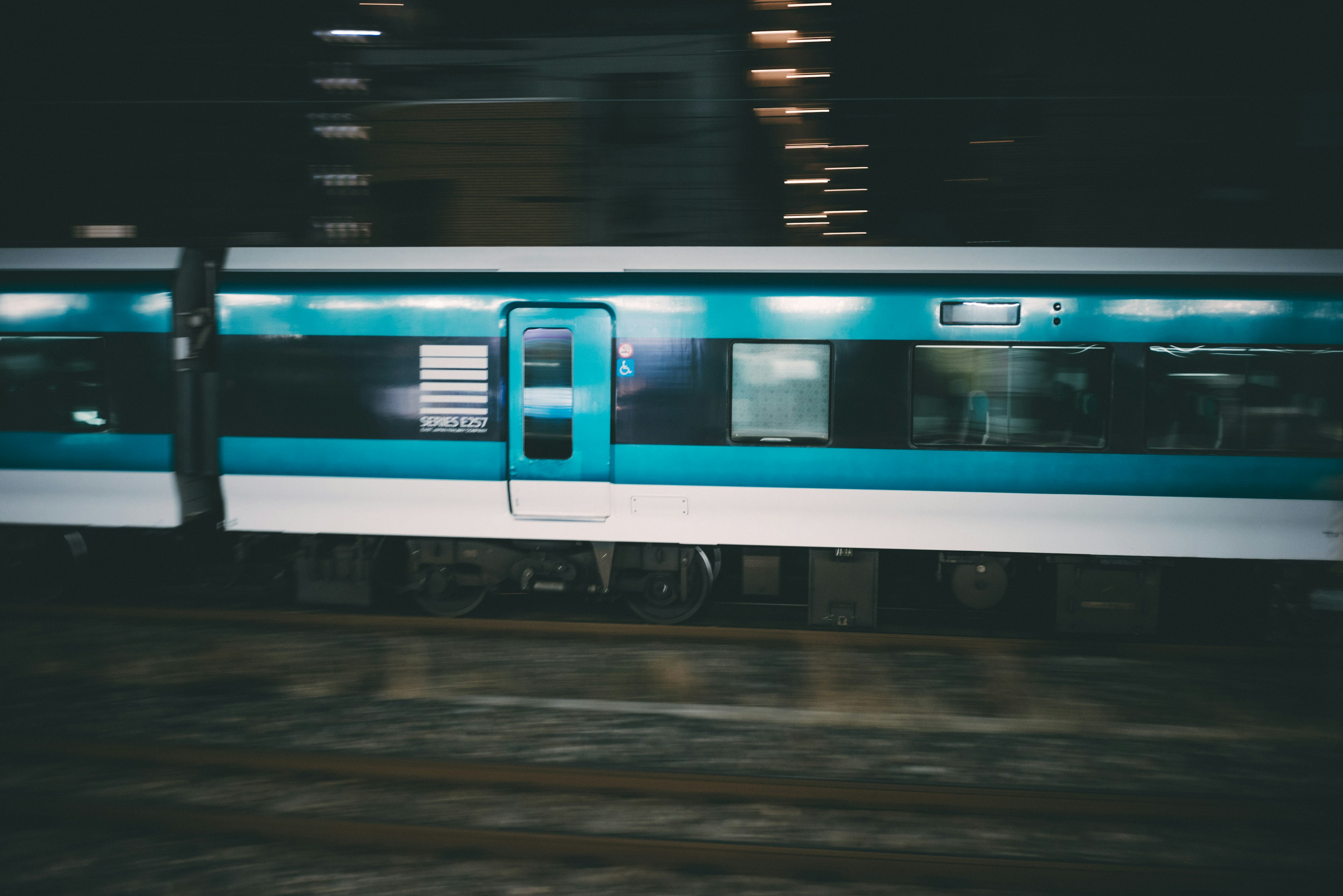 A teal train moving through a city at night